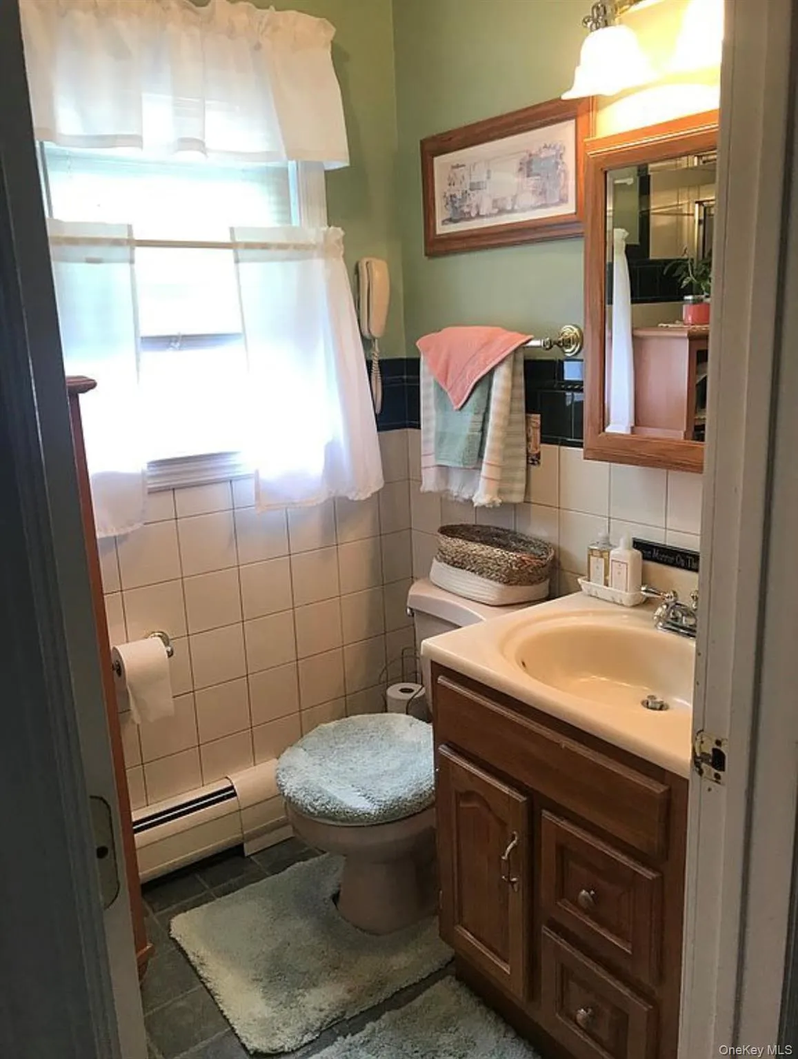 Half bathroom with vanity, baseboard heating, tile walls, and dark tile patterned flooring Half bathroom with vanity, baseboard heating, tile walls, and dark tile patterned flooring