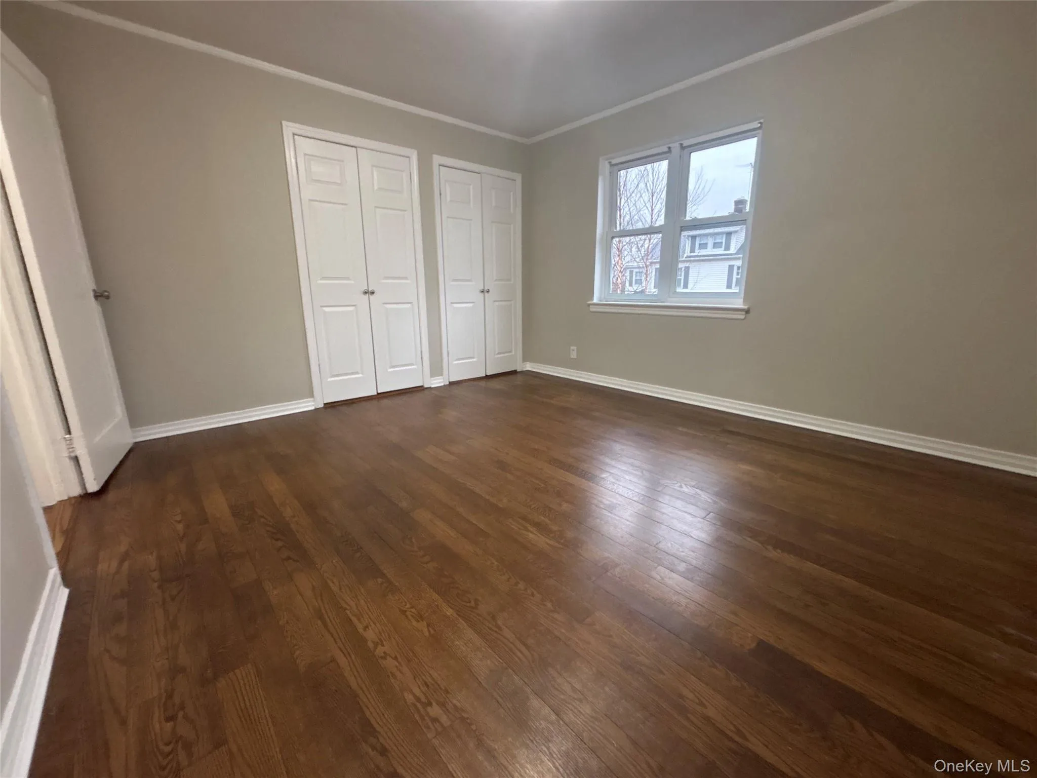 Unfurnished bedroom featuring multiple closets, crown molding, and dark wood-type flooring Unfurnished bedroom featuring multiple closets, crown molding, and dark wood-type flooring