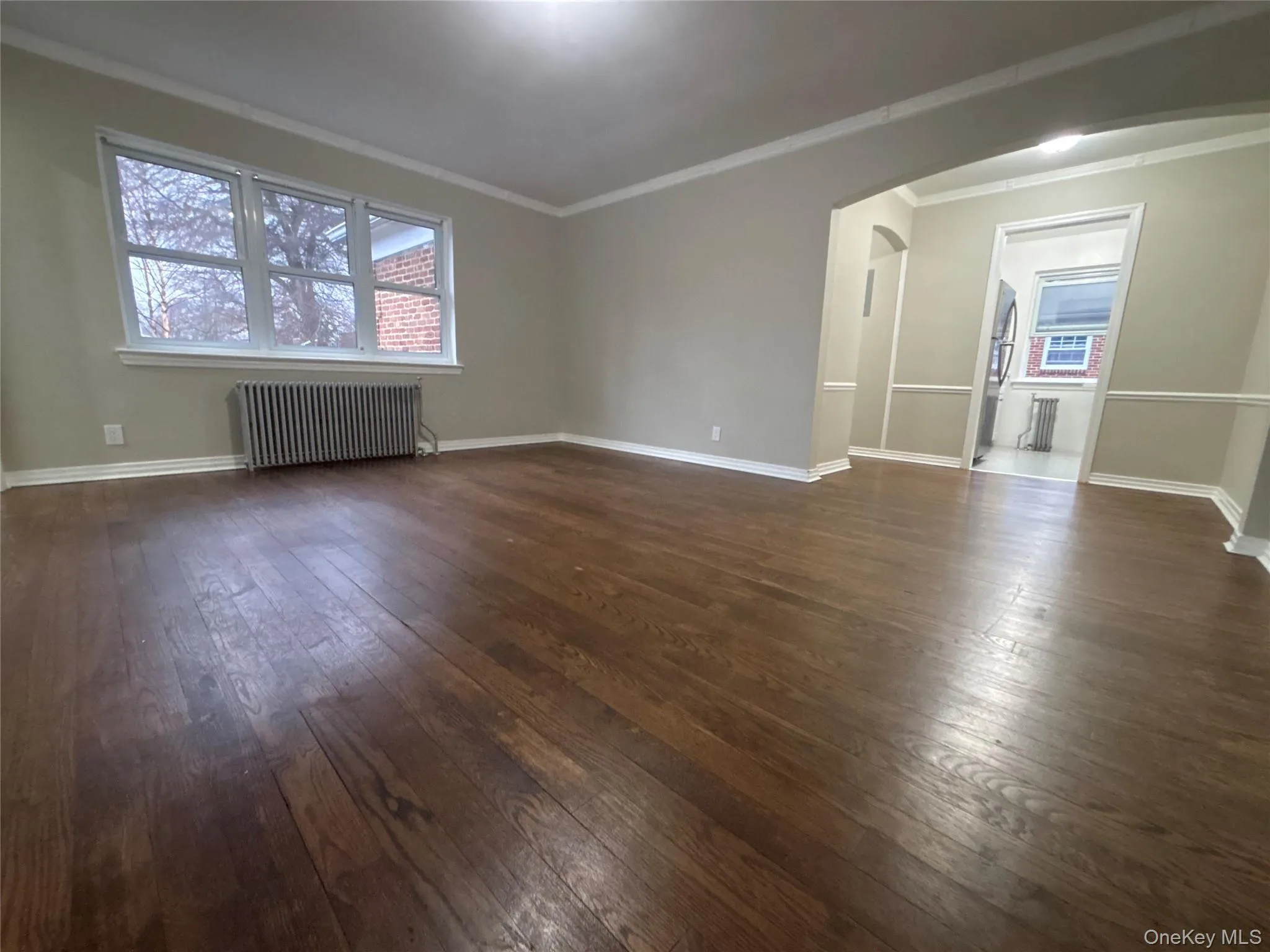 Empty room with arched walkways, radiator, ornamental molding, and dark wood finished floors Empty room with arched walkways, radiator, ornamental molding, and dark wood finished floors