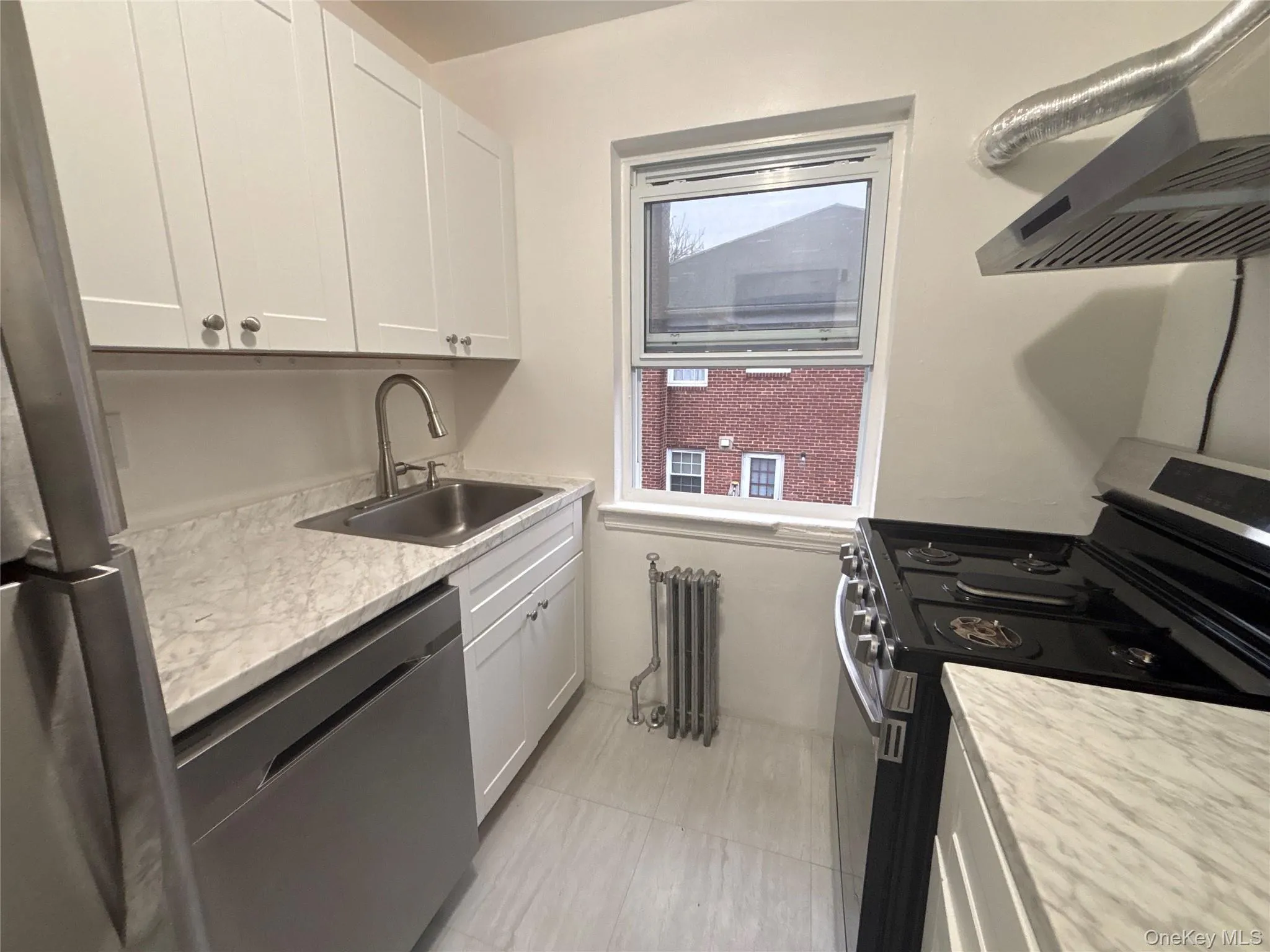 Kitchen featuring stainless steel appliances, range hood, white cabinets, and radiator Kitchen featuring stainless steel appliances, range hood, white cabinets, and radiator