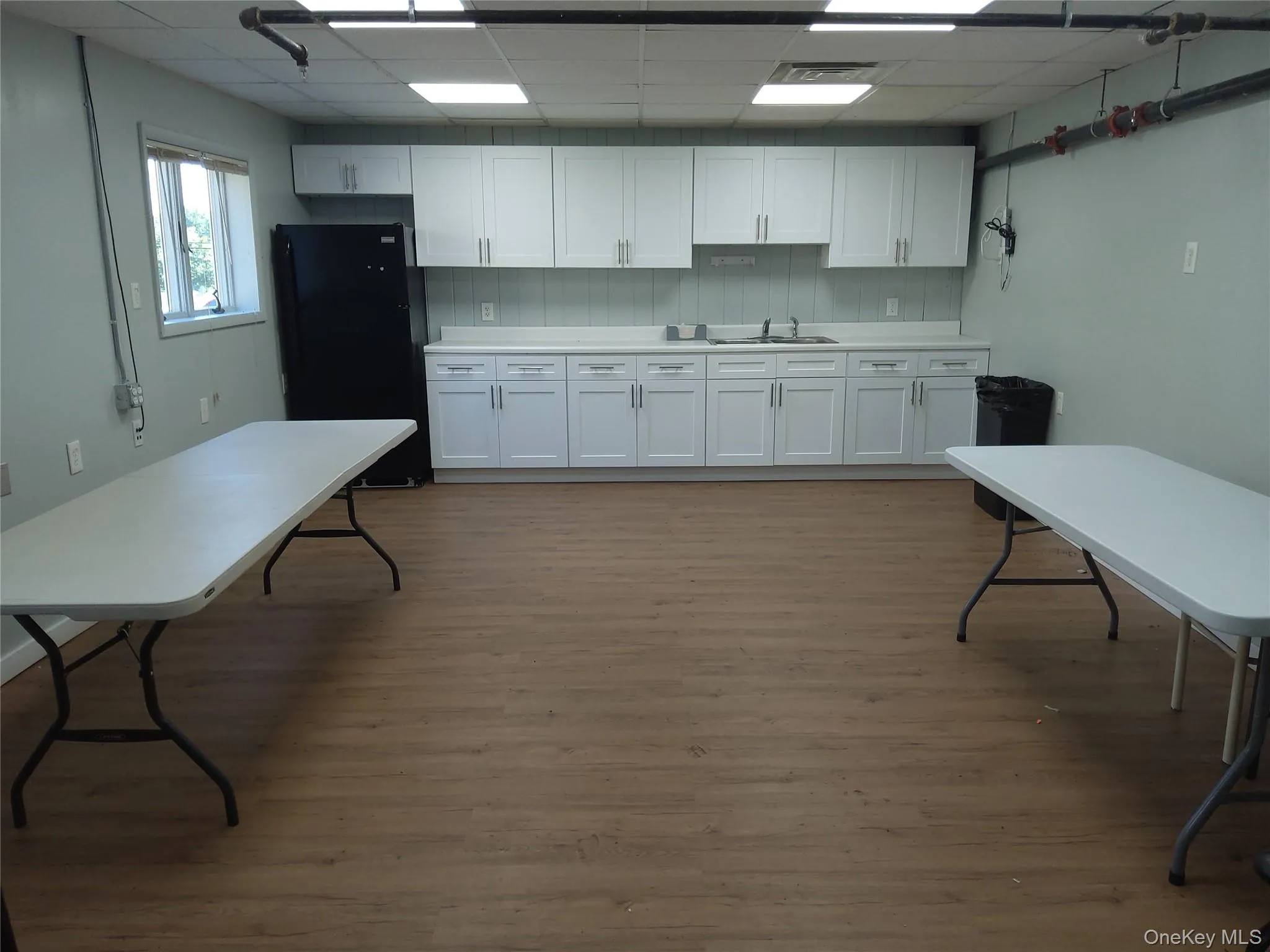 Kitchen with light wood-style floors, freestanding refrigerator, white cabinets, a drop ceiling, and light countertops Kitchen with light wood-style floors, freestanding refrigerator, white cabinets, a drop ceiling, and light countertops