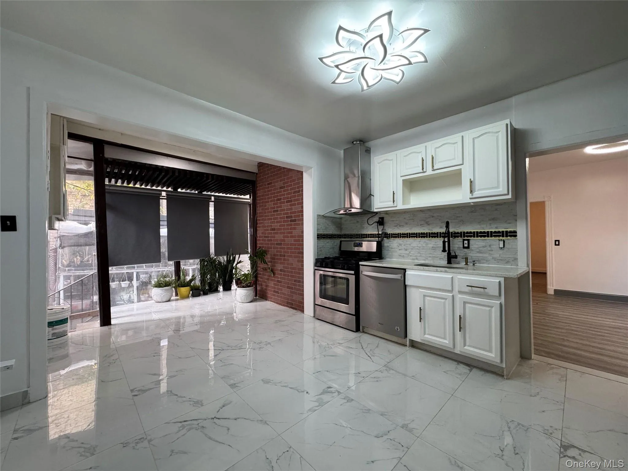 Kitchen with white cabinets, light marble finish floors, appliances with stainless steel finishes, decorative backsplash, and wall chimney exhaust hood Kitchen with white cabinets, light marble finish floors, appliances with stainless steel finishes, decorative backsplash, and wall chimney exhaust hood