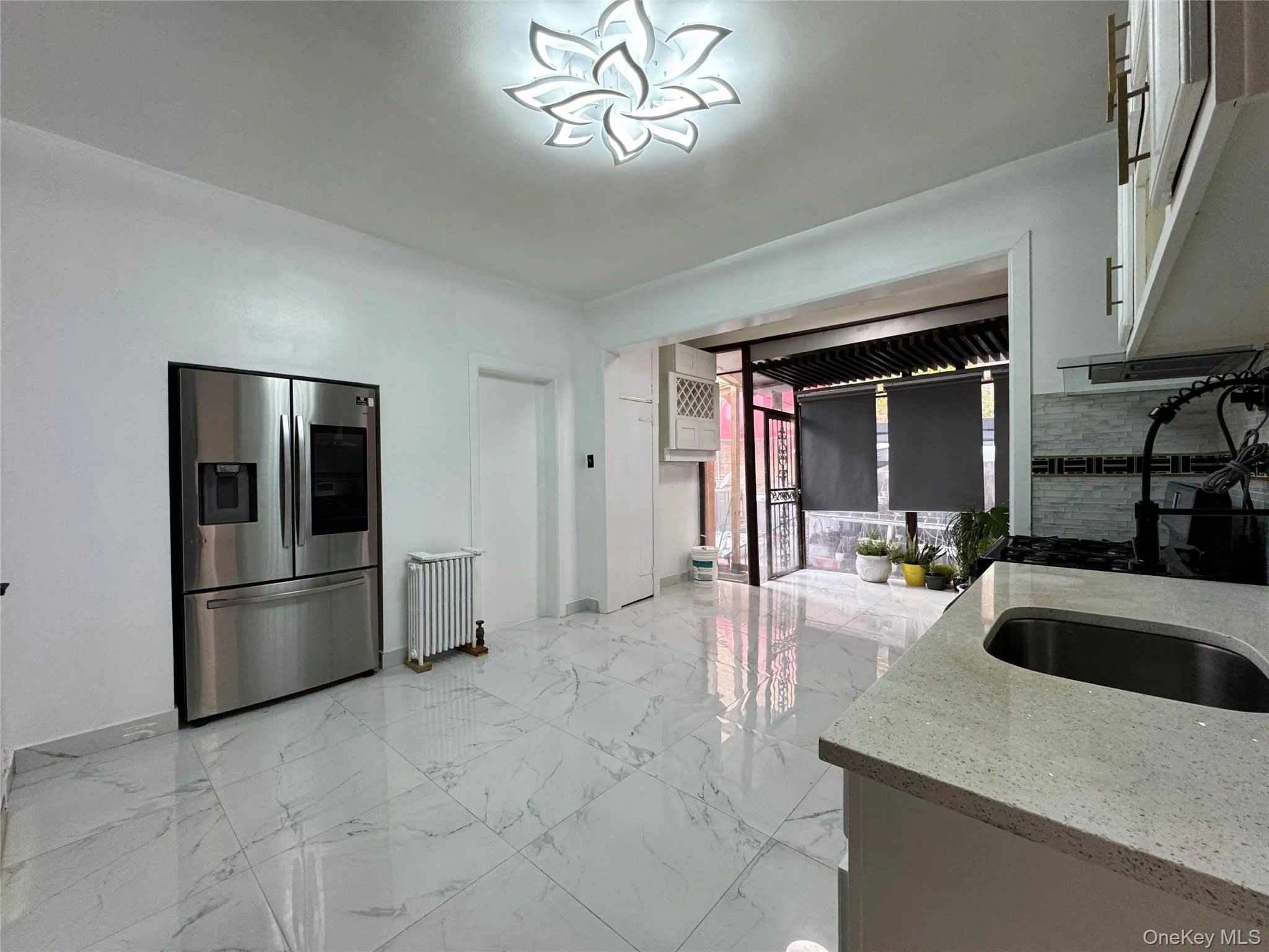 Kitchen with stainless steel refrigerator with ice dispenser, light marble finish floors, light stone countertops, radiator, and white cabinetry Kitchen with stainless steel refrigerator with ice dispenser, light marble finish floors, light stone countertops, radiator, and white cabinetry