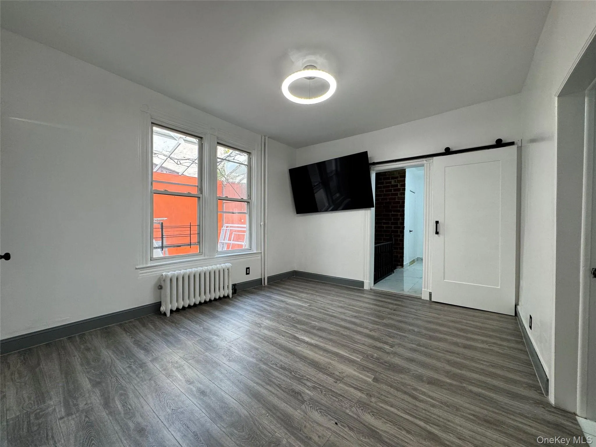 Unfurnished bedroom featuring a barn door, dark wood-style floors, radiator heating unit, and connected bathroom Unfurnished bedroom featuring a barn door, dark wood-style floors, radiator heating unit, and connected bathroom