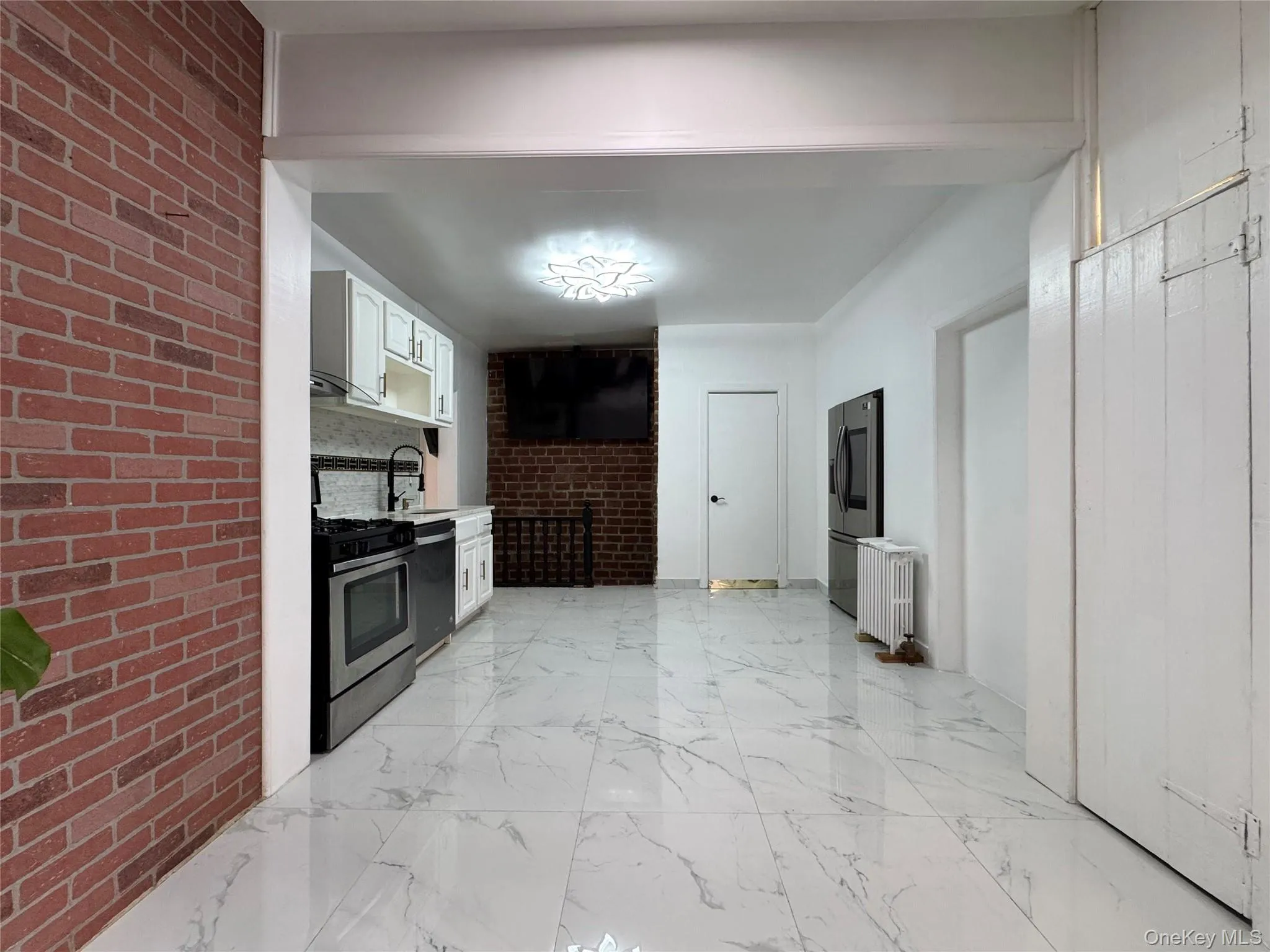 Kitchen featuring light countertops, white cabinets, stainless steel appliances, brick wall, and light marble finish flooring Kitchen featuring light countertops, white cabinets, stainless steel appliances, brick wall, and light marble finish flooring
