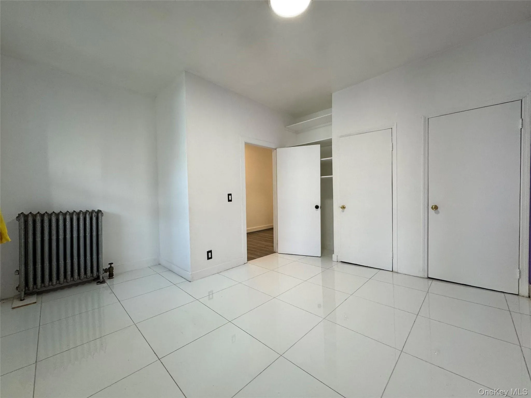 Unfurnished bedroom featuring radiator and light tile patterned flooring Unfurnished bedroom featuring radiator and light tile patterned flooring