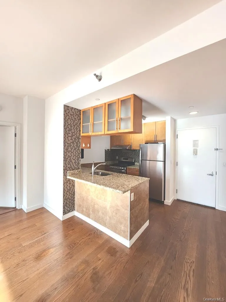Kitchen featuring appliances with stainless steel finishes, glass insert cabinets, a peninsula, and dark wood-style floors Kitchen featuring appliances with stainless steel finishes, glass insert cabinets, a peninsula, and dark wood-style floors