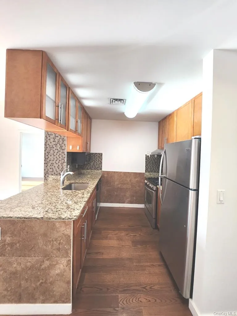 Kitchen featuring dark wood-type flooring, glass insert cabinets, decorative backsplash, stainless steel appliances, and light stone counters Kitchen featuring dark wood-type flooring, glass insert cabinets, decorative backsplash, stainless steel appliances, and light stone counters