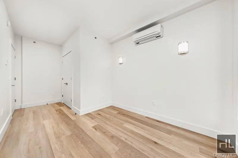 Unfurnished room featuring a wall mounted air conditioner and light wood-style floors Unfurnished room featuring a wall mounted air conditioner and light wood-style floors