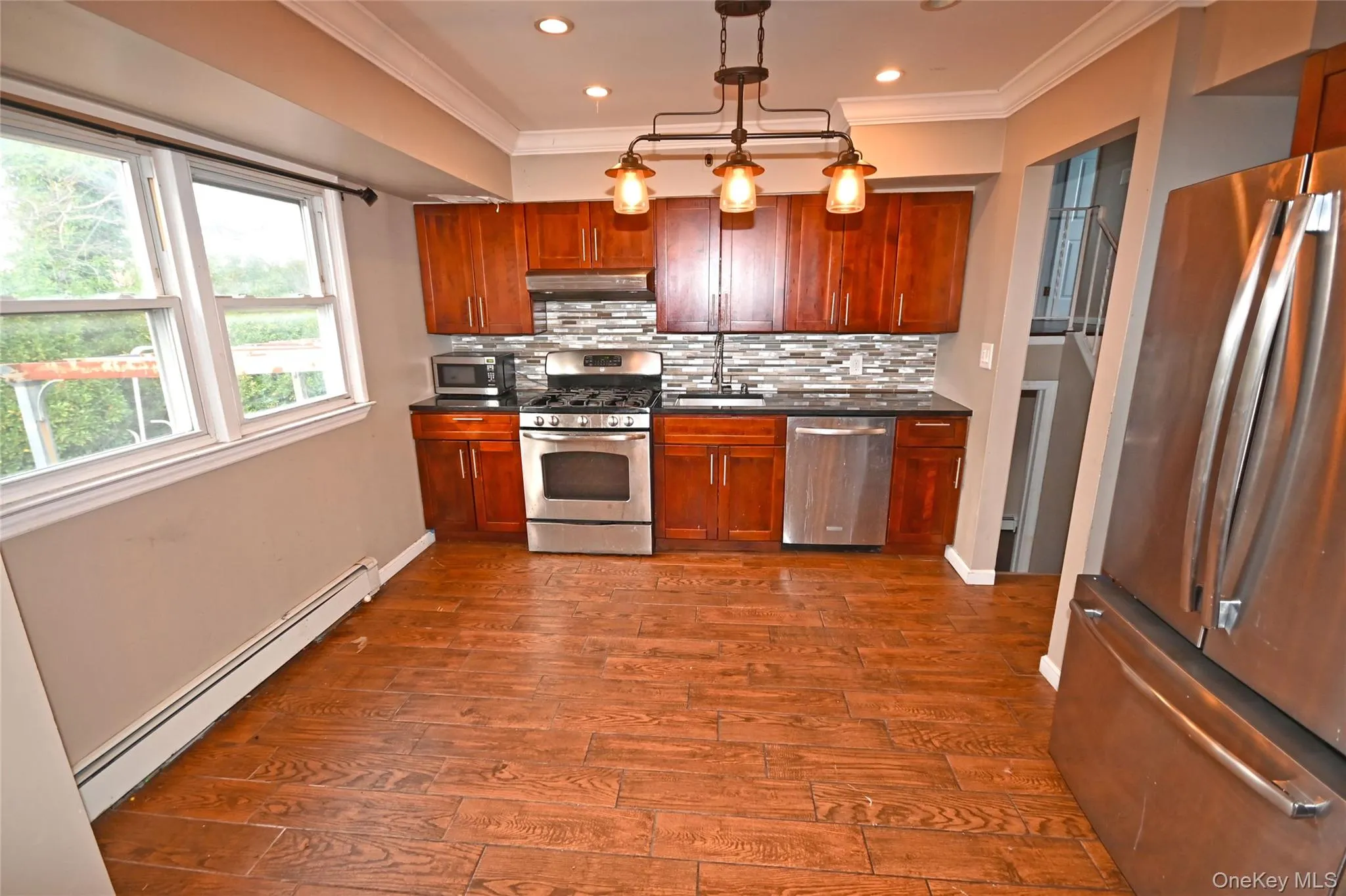 Kitchen with appliances with stainless steel finishes, a baseboard radiator, tasteful backsplash, hanging light fixtures, and dark wood finished floors Kitchen with appliances with stainless steel finishes, a baseboard radiator, tasteful backsplash, hanging light fixtures, and dark wood finished floors