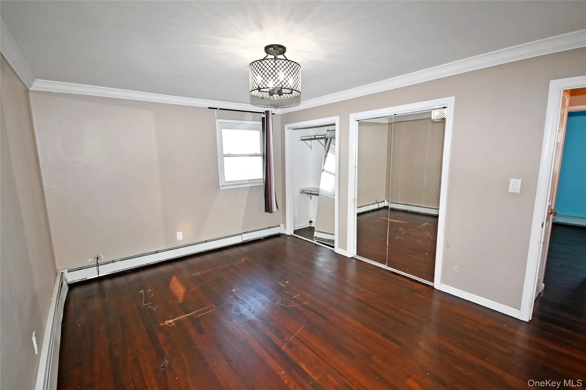 Unfurnished bedroom with two closets, dark wood-type flooring, ornamental molding, and a baseboard heating unit Unfurnished bedroom with two closets, dark wood-type flooring, ornamental molding, and a baseboard heating unit