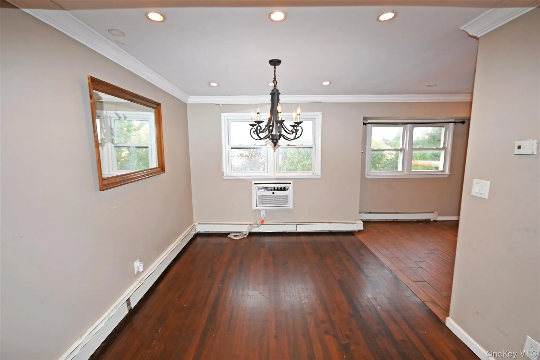 Unfurnished dining area featuring a baseboard radiator, healthy amount of natural light, crown molding, dark wood-type flooring, and a chandelier Unfurnished dining area featuring a baseboard radiator, healthy amount of natural light, crown molding, dark wood-type flooring, and a chandelier