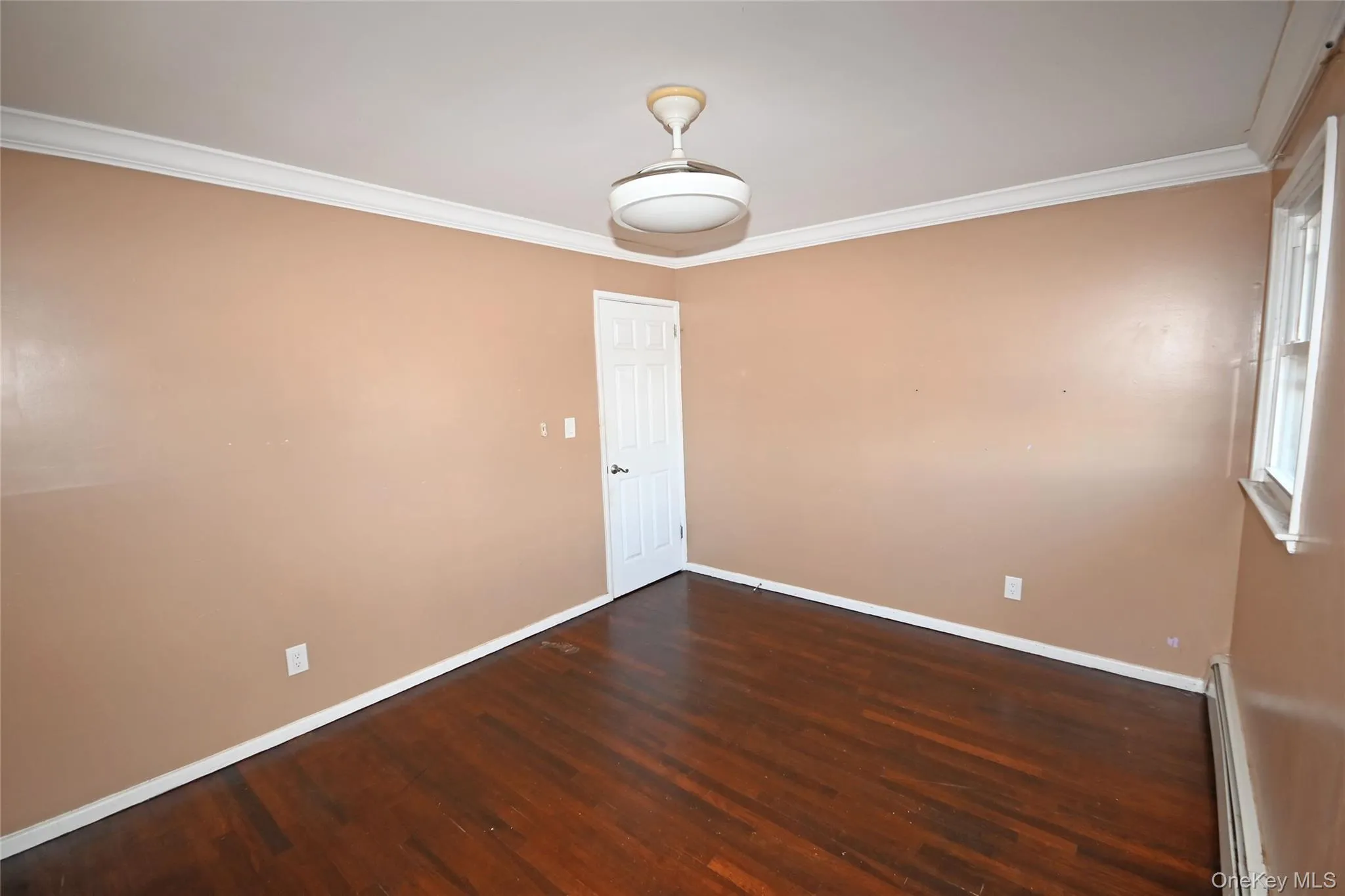 Empty room with ornamental molding, dark wood-style floors, and a baseboard heating unit Empty room with ornamental molding, dark wood-style floors, and a baseboard heating unit
