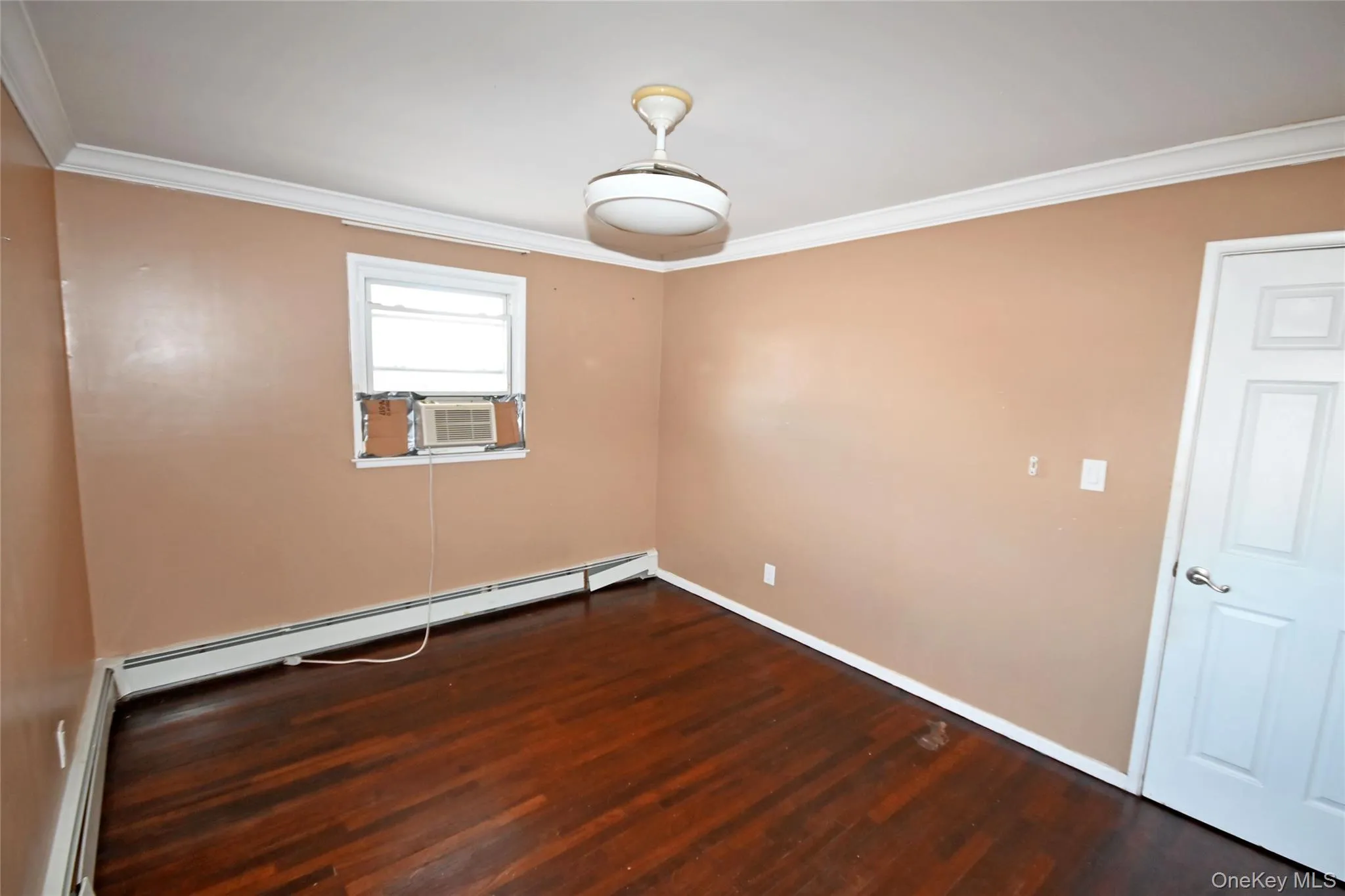 Empty room featuring crown molding, dark wood-style floors, baseboard heating, and cooling unit Empty room featuring crown molding, dark wood-style floors, baseboard heating, and cooling unit