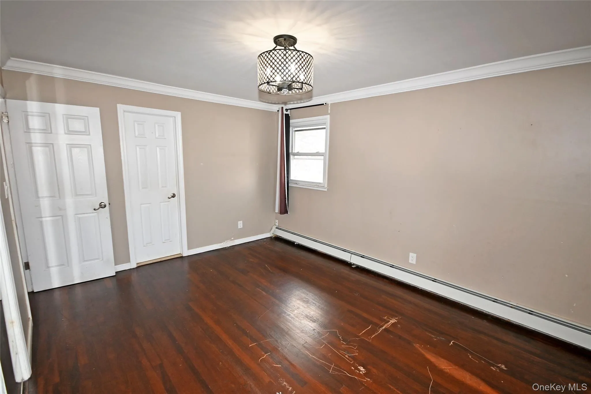 Unfurnished bedroom featuring baseboard heating, ornamental molding, and dark wood-type flooring Unfurnished bedroom featuring baseboard heating, ornamental molding, and dark wood-type flooring