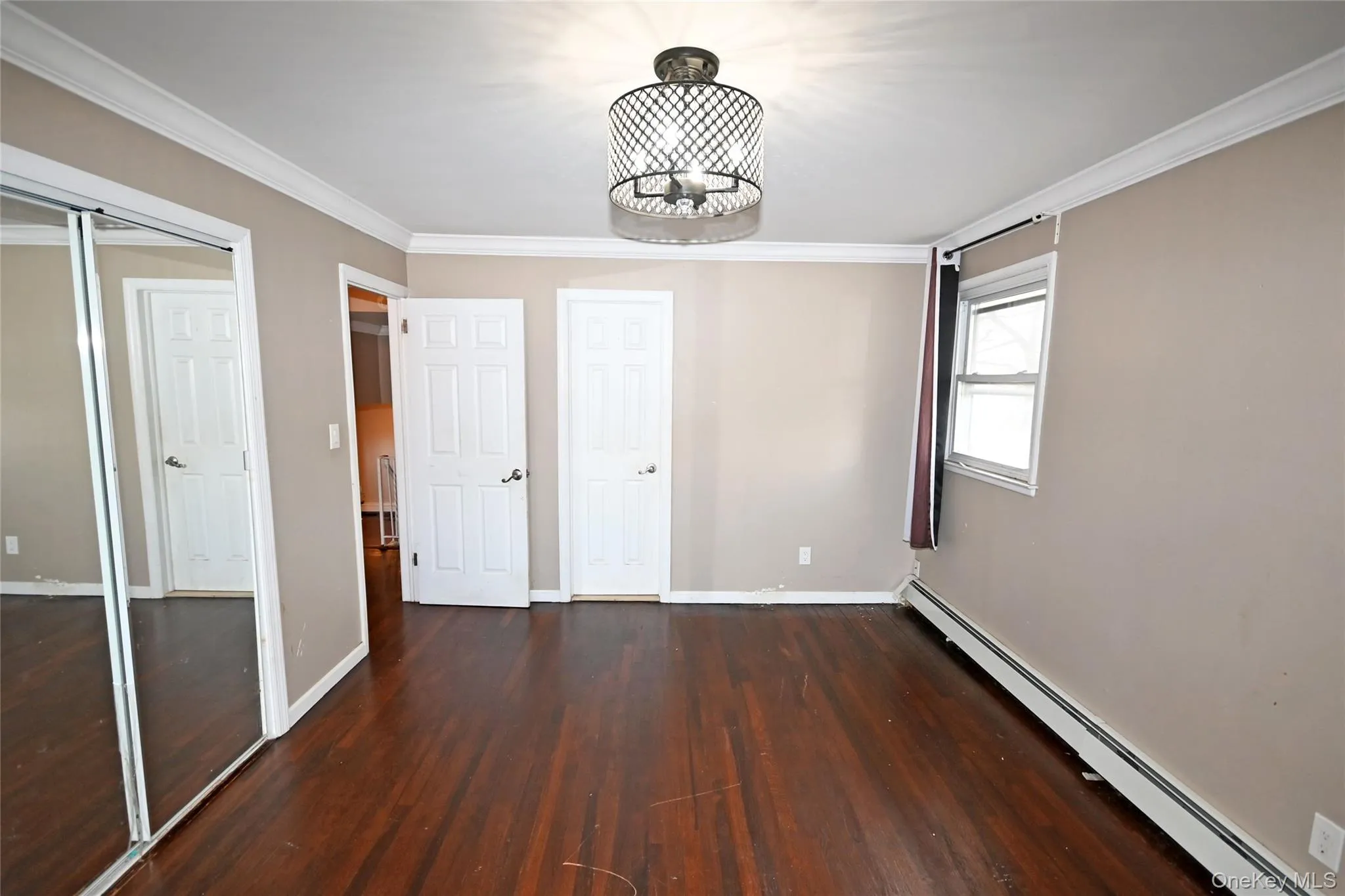 Unfurnished bedroom featuring a baseboard heating unit, dark wood-style floors, ornamental molding, a closet, and a chandelier Unfurnished bedroom featuring a baseboard heating unit, dark wood-style floors, ornamental molding, a closet, and a chandelier