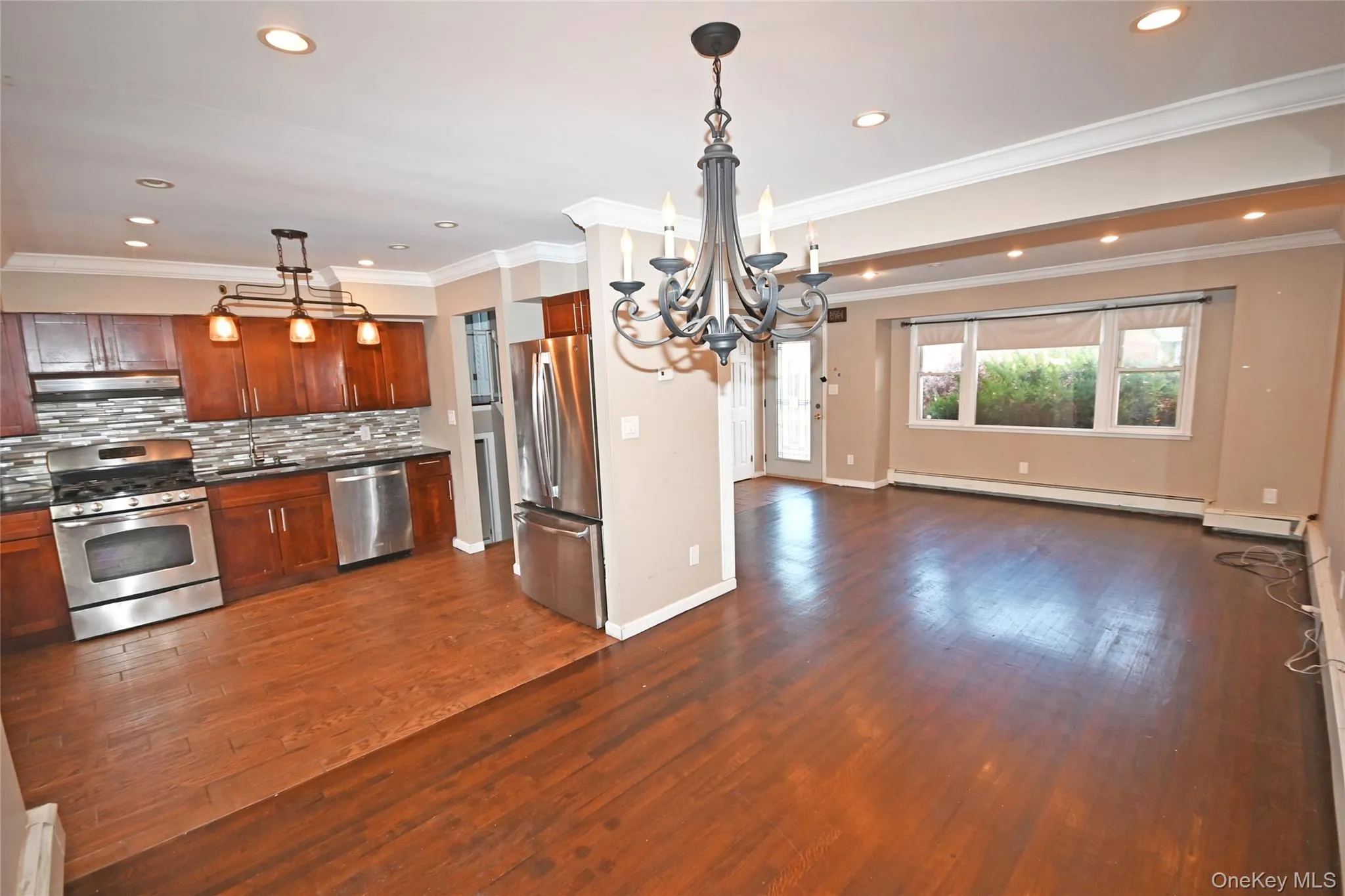 Kitchen featuring ornamental molding, appliances with stainless steel finishes, decorative light fixtures, dark wood-style floors, and a chandelier Kitchen featuring ornamental molding, appliances with stainless steel finishes, decorative light fixtures, dark wood-style floors, and a chandelier
