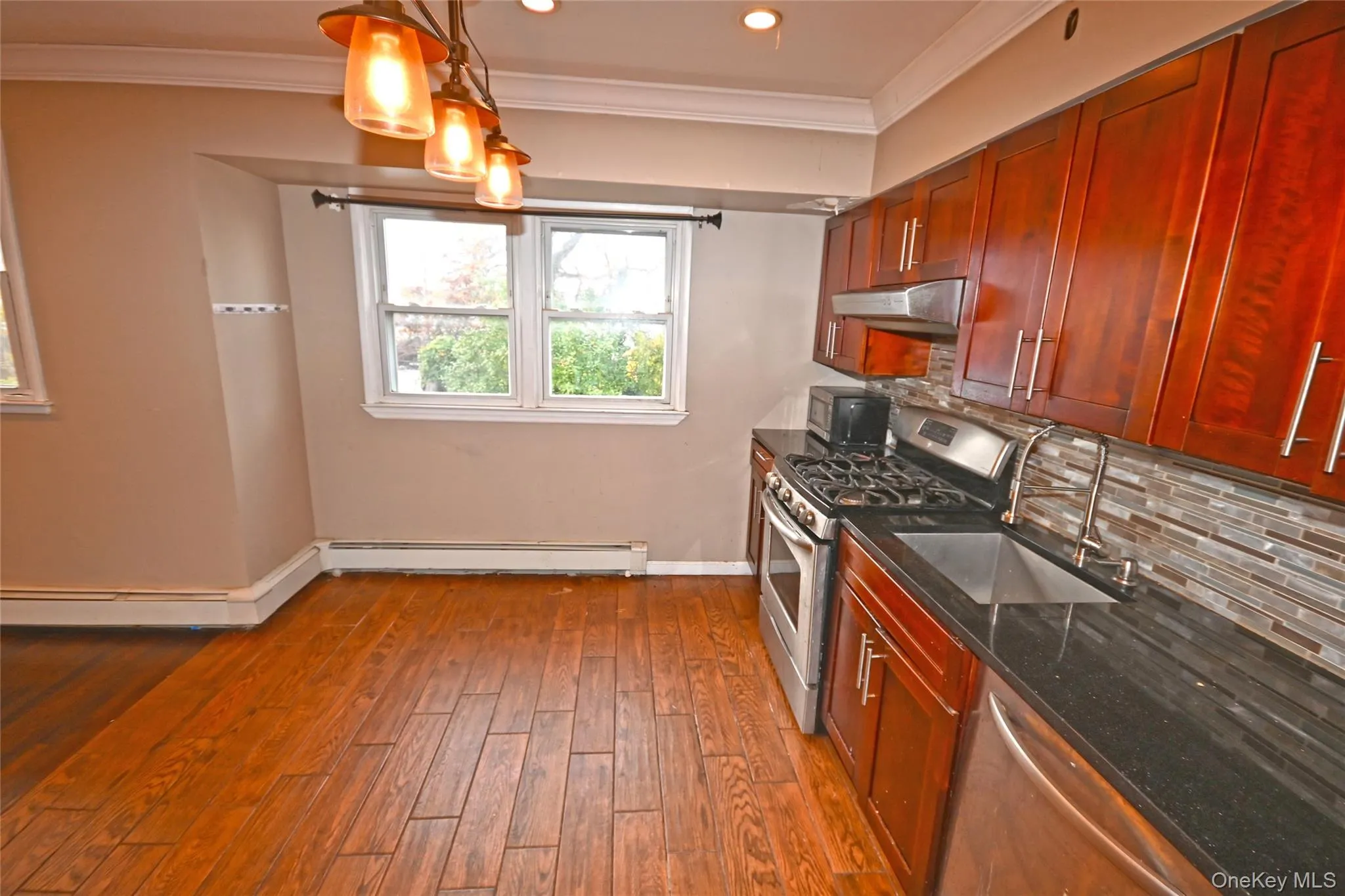 Kitchen featuring stainless steel appliances, dark stone countertops, crown molding, decorative backsplash, and hanging light fixtures Kitchen featuring stainless steel appliances, dark stone countertops, crown molding, decorative backsplash, and hanging light fixtures