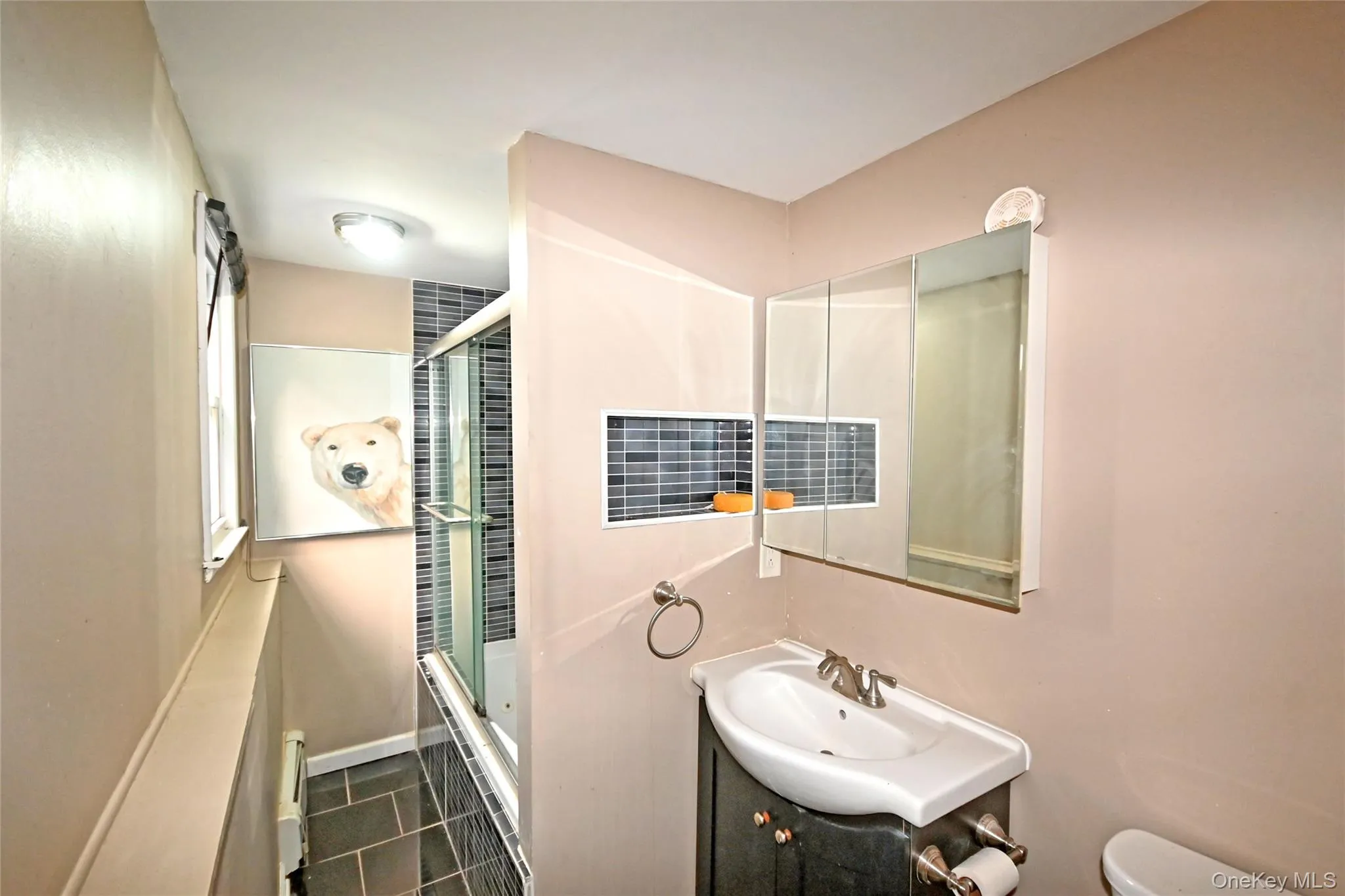 Bathroom featuring dark tile patterned flooring, bath / shower combo with glass door, and vanity Bathroom featuring dark tile patterned flooring, bath / shower combo with glass door, and vanity