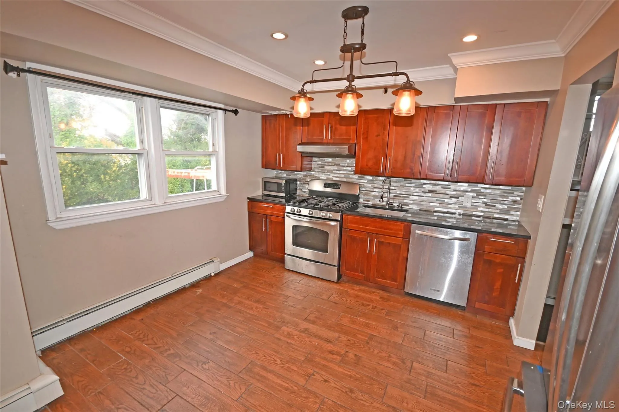 Kitchen with a baseboard radiator, appliances with stainless steel finishes, decorative light fixtures, dark wood-style flooring, and decorative backsplash Kitchen with a baseboard radiator, appliances with stainless steel finishes, decorative light fixtures, dark wood-style flooring, and decorative backsplash