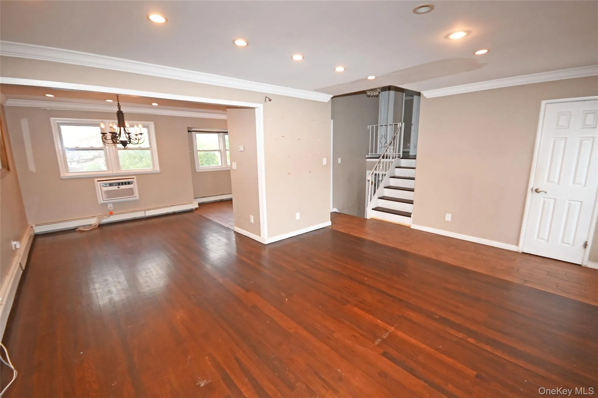 Unfurnished living room with crown molding, recessed lighting, stairway, a wall mounted air conditioner, and dark wood-type flooring Unfurnished living room with crown molding, recessed lighting, stairway, a wall mounted air conditioner, and dark wood-type flooring