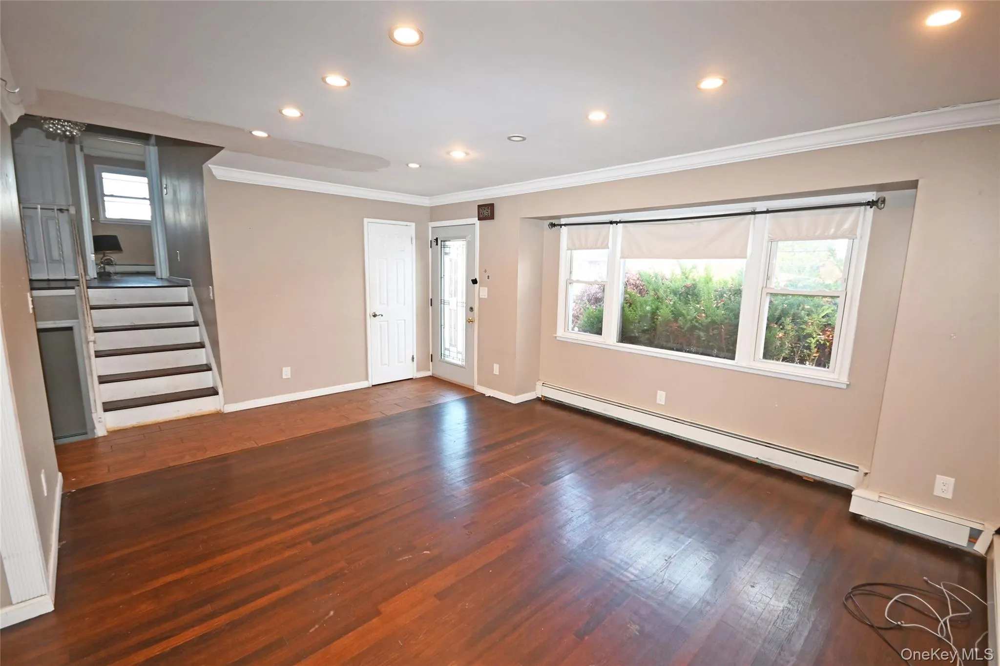 Unfurnished living room with stairs, ornamental molding, recessed lighting, dark wood-style flooring, and a baseboard heating unit Unfurnished living room with stairs, ornamental molding, recessed lighting, dark wood-style flooring, and a baseboard heating unit