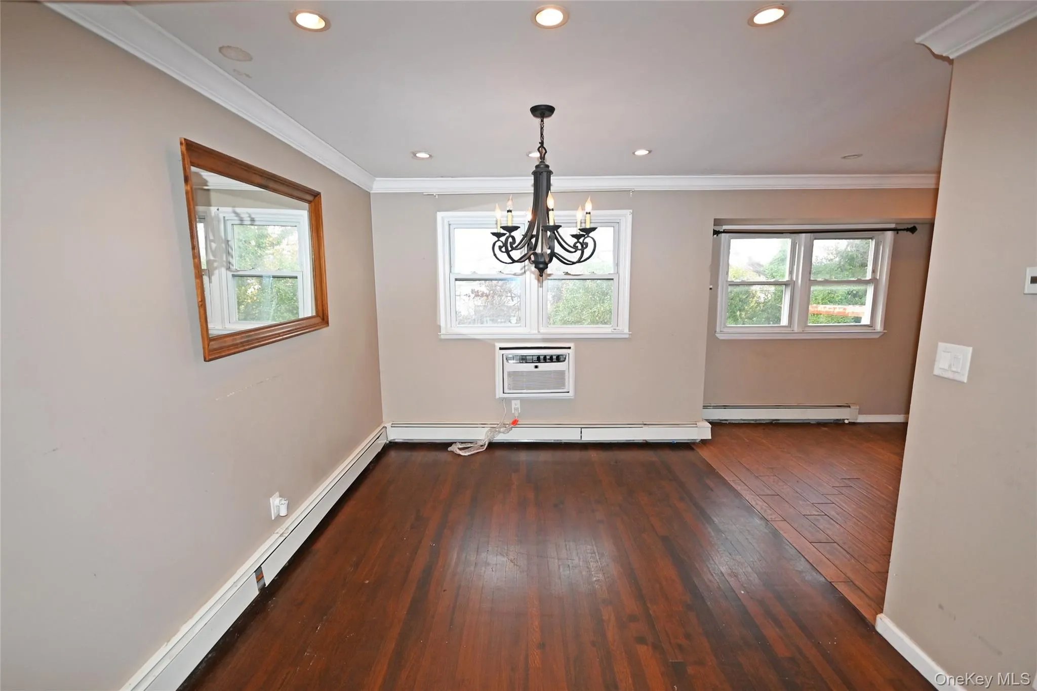 Unfurnished dining area with a baseboard heating unit, crown molding, dark wood-style flooring, a chandelier, and a wall mounted AC Unfurnished dining area with a baseboard heating unit, crown molding, dark wood-style flooring, a chandelier, and a wall mounted AC