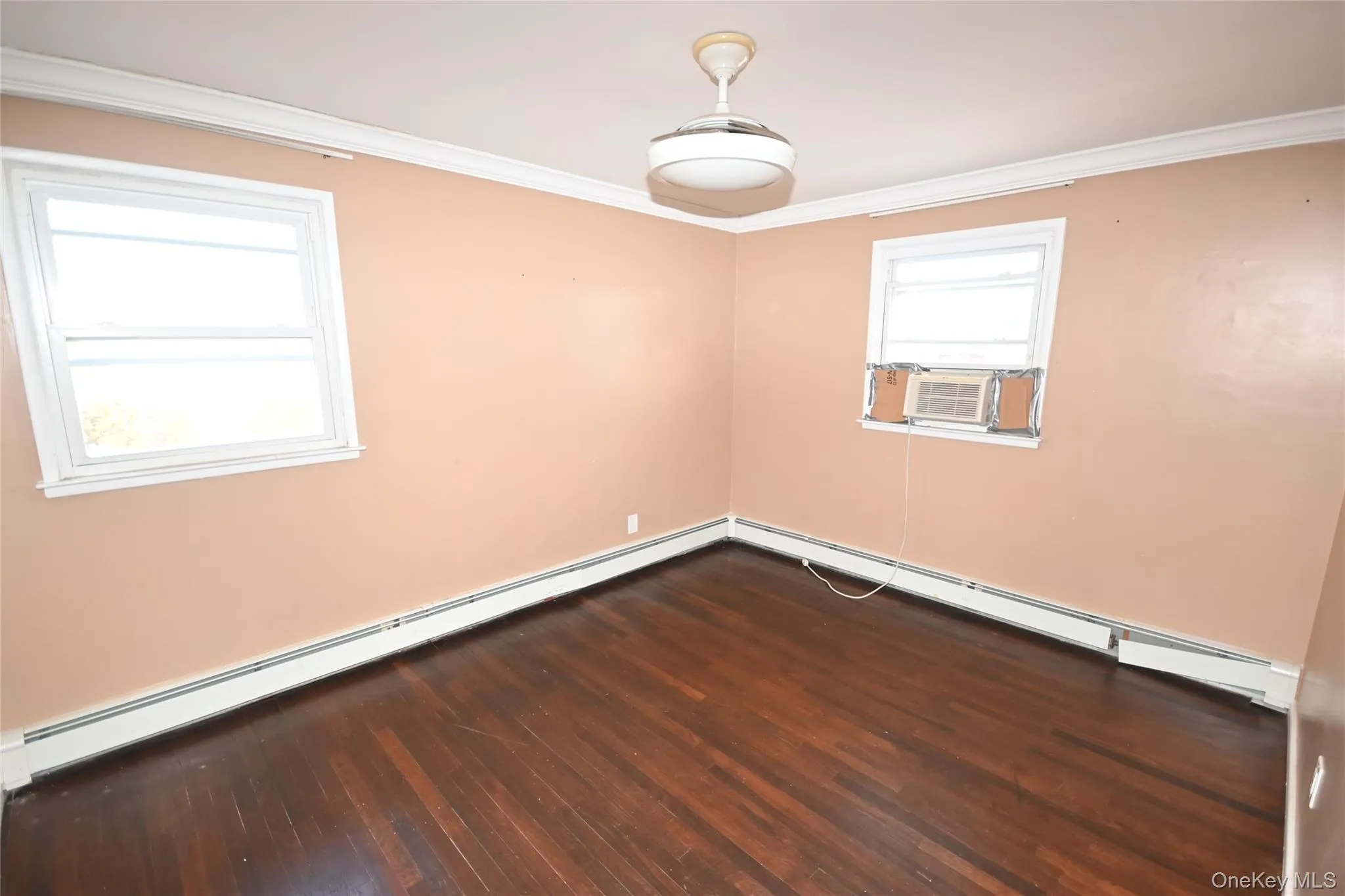 Empty room featuring a baseboard heating unit, dark wood-style floors, ornamental molding, and cooling unit Empty room featuring a baseboard heating unit, dark wood-style floors, ornamental molding, and cooling unit