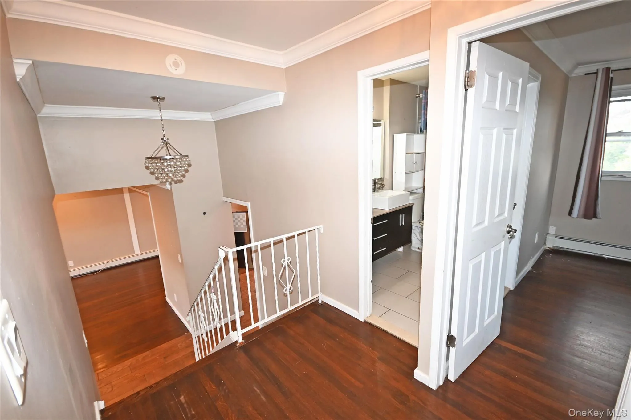 Hallway with an upstairs landing, ornamental molding, dark wood-style floors, a chandelier, and a baseboard heating unit Hallway with an upstairs landing, ornamental molding, dark wood-style floors, a chandelier, and a baseboard heating unit
