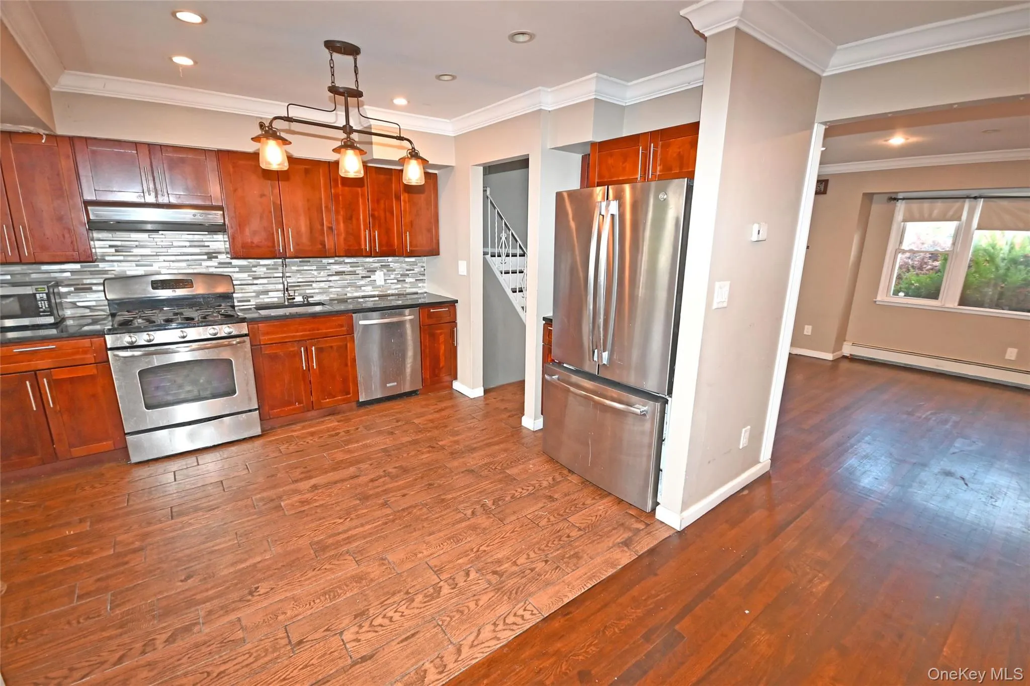 Kitchen featuring crown molding, stainless steel appliances, decorative backsplash, pendant lighting, and dark wood-type flooring Kitchen featuring crown molding, stainless steel appliances, decorative backsplash, pendant lighting, and dark wood-type flooring