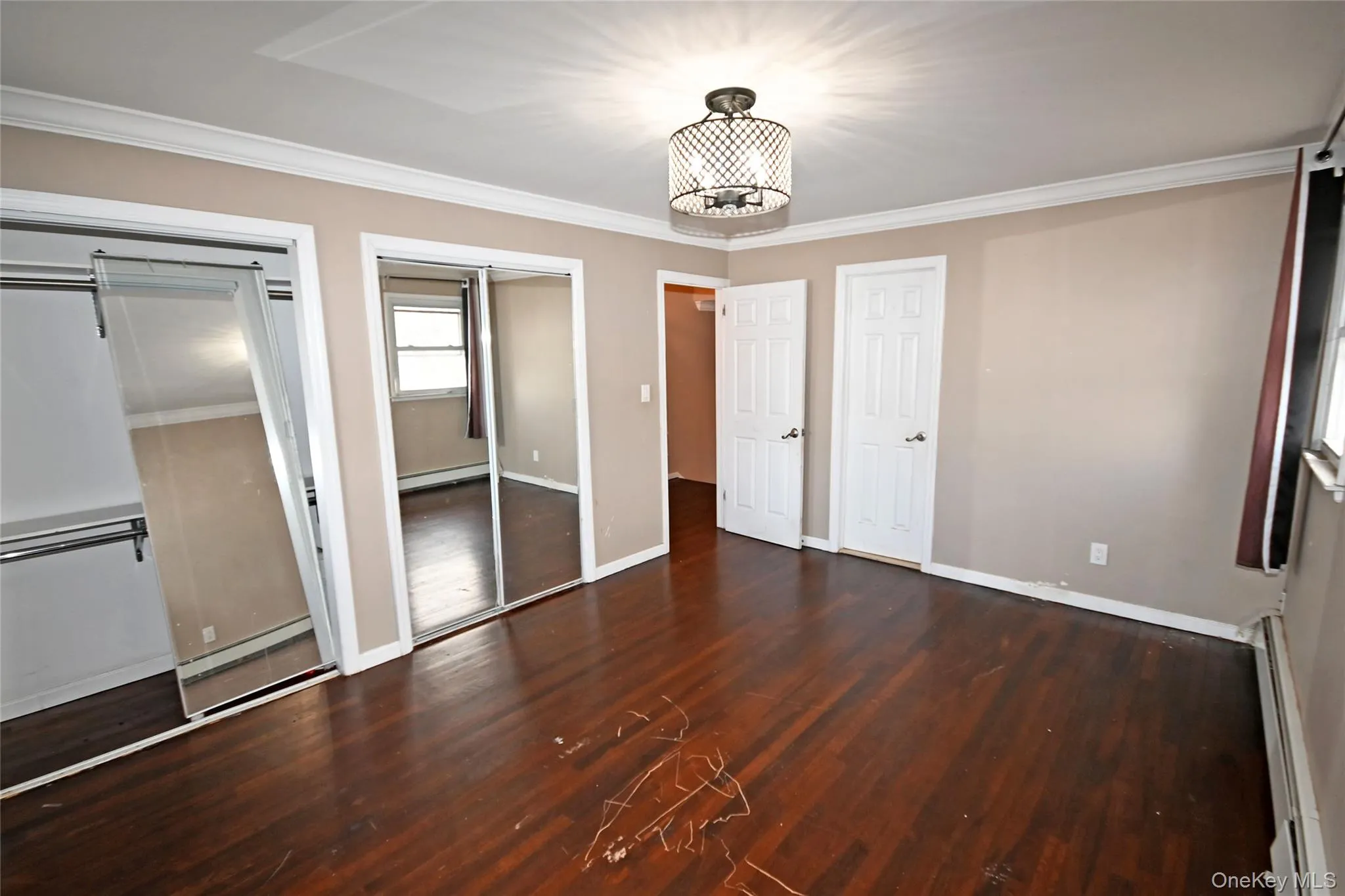 Unfurnished bedroom with two closets, ornamental molding, dark wood-style floors, and baseboard heating Unfurnished bedroom with two closets, ornamental molding, dark wood-style floors, and baseboard heating