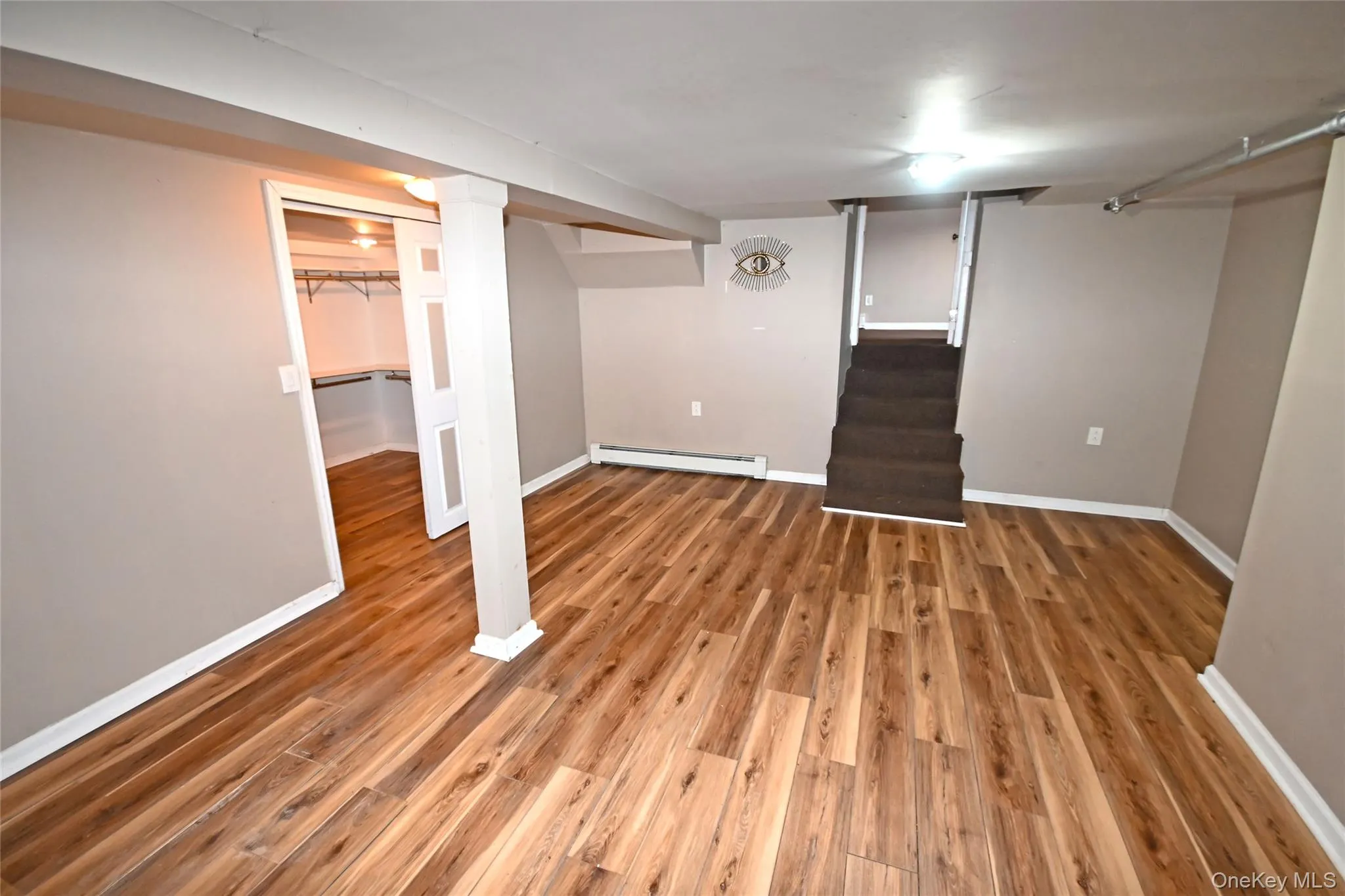 Finished below grade area featuring stairs, light wood-style floors, and a baseboard heating unit Finished below grade area featuring stairs, light wood-style floors, and a baseboard heating unit