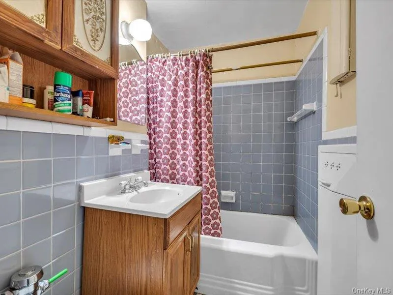 Bathroom featuring tile walls, vanity, shower / bathtub combination with curtain, and backsplash Bathroom featuring tile walls, vanity, shower / bathtub combination with curtain, and backsplash
