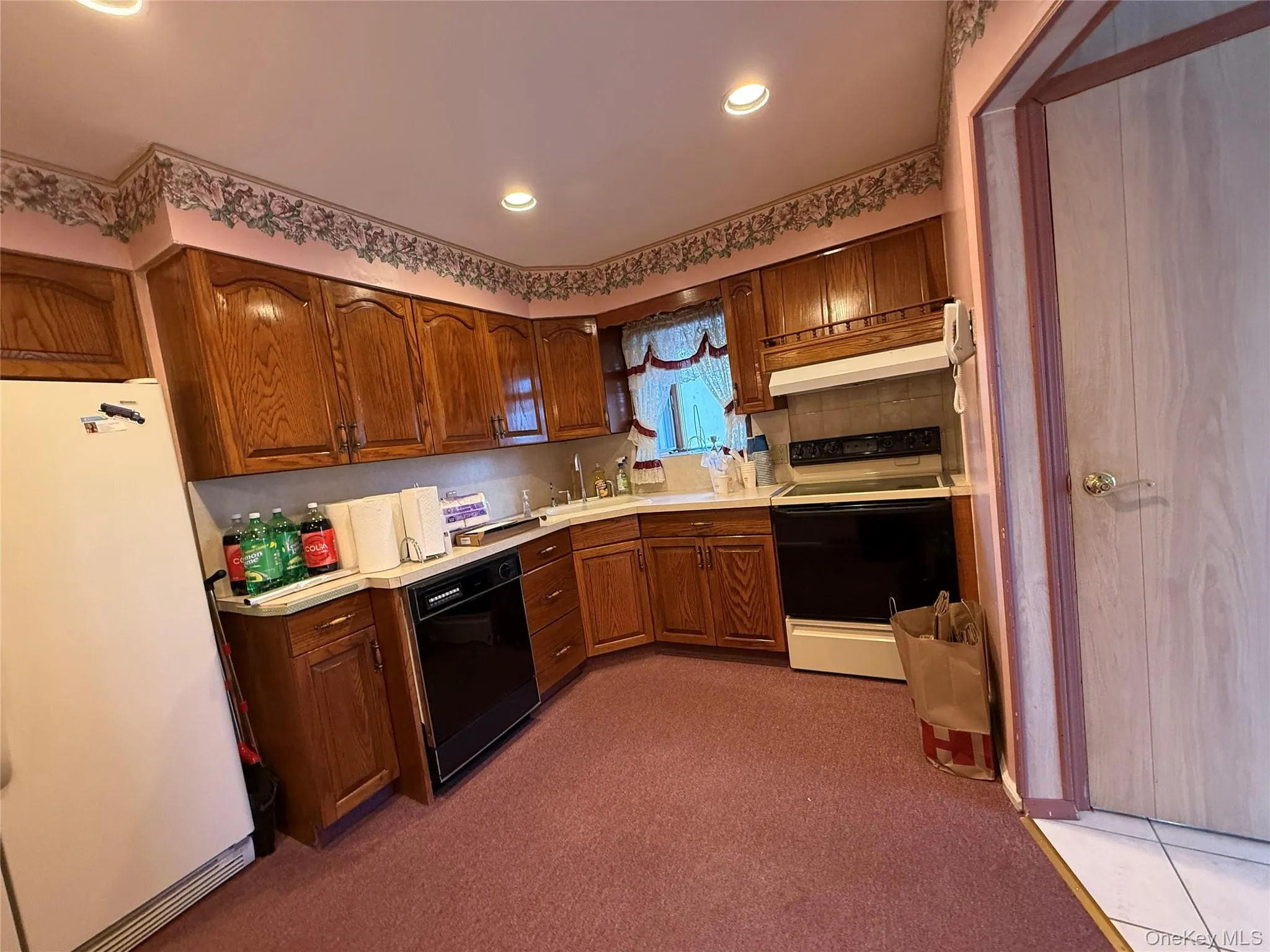 Kitchen featuring freestanding refrigerator, brown cabinets, light countertops, electric range oven, and recessed lighting Kitchen featuring freestanding refrigerator, brown cabinets, light countertops, electric range oven, and recessed lighting