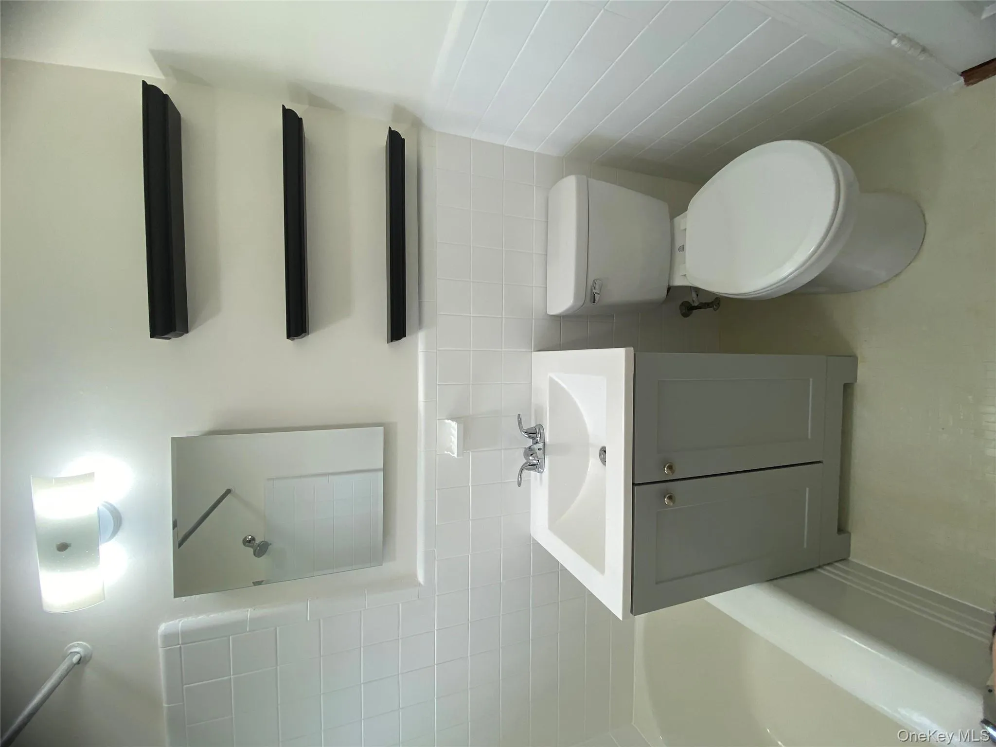 Bathroom featuring tile walls, washtub / shower combination, vanity, and a wainscoted wall Bathroom featuring tile walls, washtub / shower combination, vanity, and a wainscoted wall