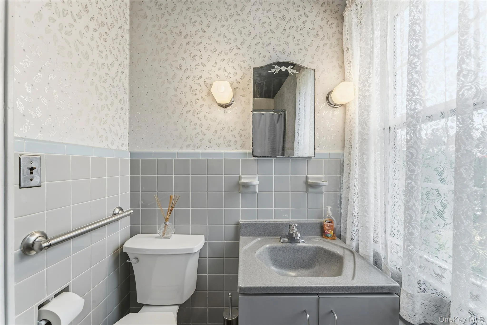Full bathroom featuring a wainscoted wall, tile walls, a shower with shower curtain, vanity, and wallpapered walls Full bathroom featuring a wainscoted wall, tile walls, a shower with shower curtain, vanity, and wallpapered walls