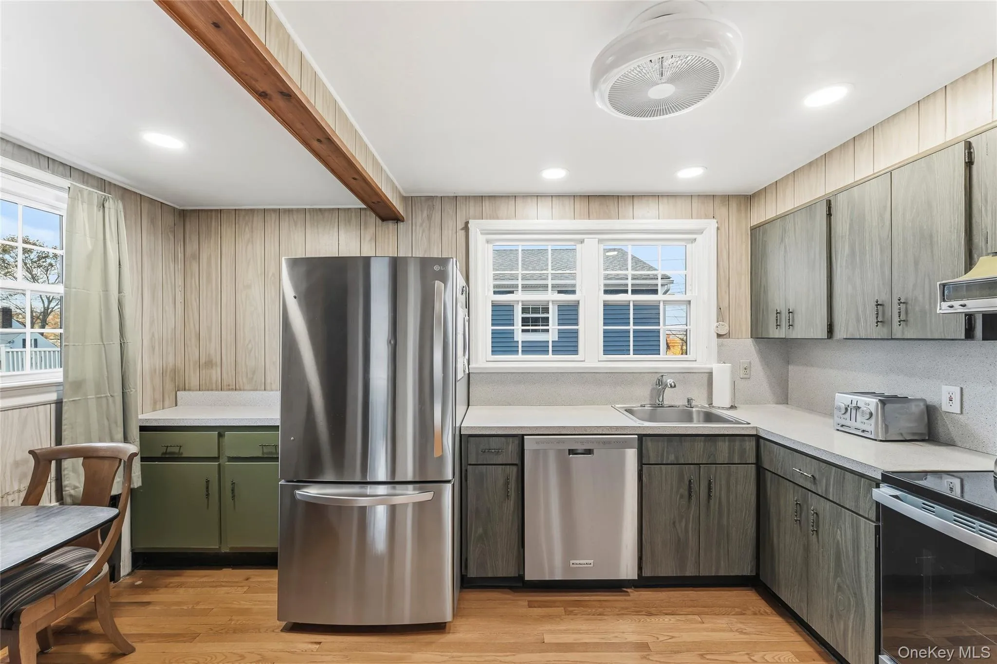 Kitchen with stainless steel appliances, light countertops, beamed ceiling, light wood-style floors, and wooden walls Kitchen with stainless steel appliances, light countertops, beamed ceiling, light wood-style floors, and wooden walls