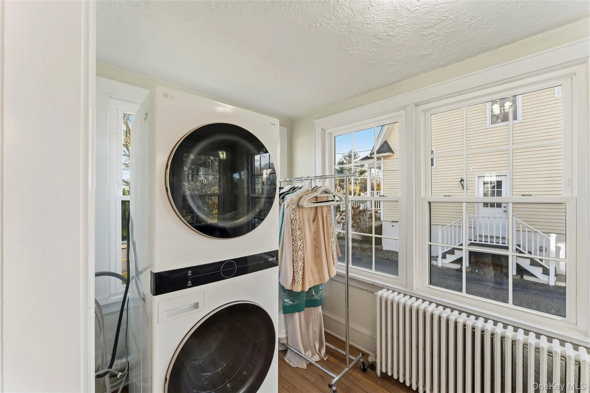 Laundry area with radiator, stacked washer / dryer, wood finished floors, and a textured ceiling Laundry area with radiator, stacked washer / dryer, wood finished floors, and a textured ceiling