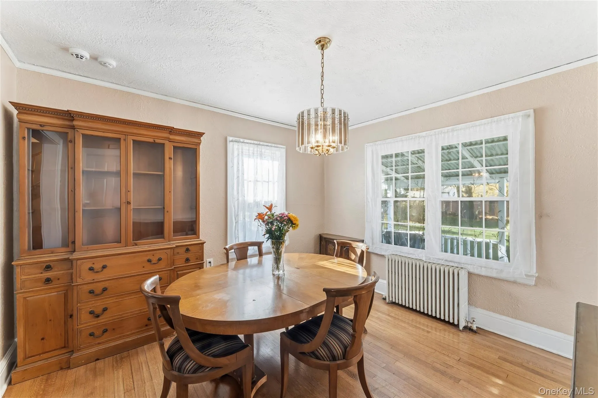 Dining room featuring radiator heating unit, a textured ceiling, light wood-style floors, ornamental molding, and a chandelier Dining room featuring radiator heating unit, a textured ceiling, light wood-style floors, ornamental molding, and a chandelier