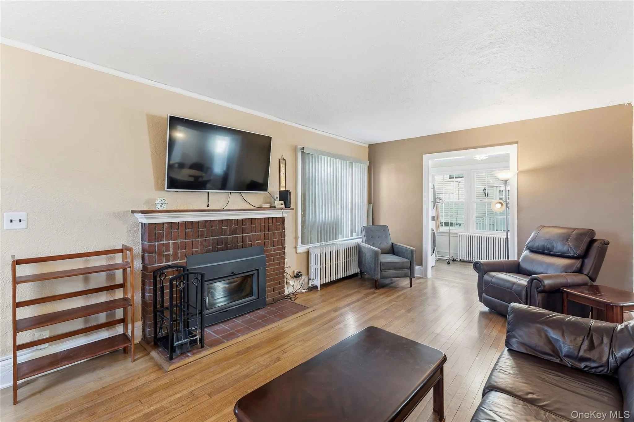 Living area with hardwood / wood-style floors, radiator, and a brick fireplace Living area with hardwood / wood-style floors, radiator, and a brick fireplace