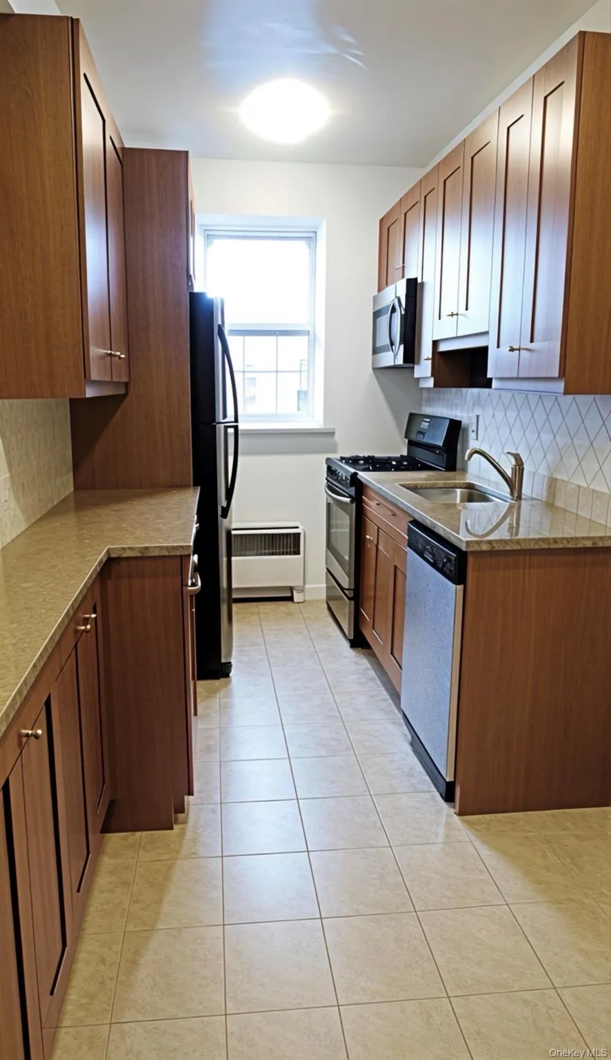 Kitchen with tasteful backsplash, stainless steel appliances, light tile patterned floors, radiator heating unit, and light stone countertops Kitchen with tasteful backsplash, stainless steel appliances, light tile patterned floors, radiator heating unit, and light stone countertops