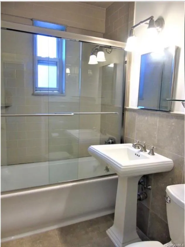 Full bath featuring combined bath / shower with glass door, tile walls, and tasteful backsplash Full bath featuring combined bath / shower with glass door, tile walls, and tasteful backsplash