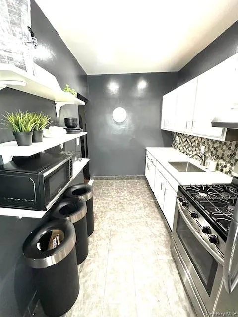 Kitchen featuring stainless steel gas stove, white cabinetry, black microwave, backsplash, and extractor fan Kitchen featuring stainless steel gas stove, white cabinetry, black microwave, backsplash, and extractor fan