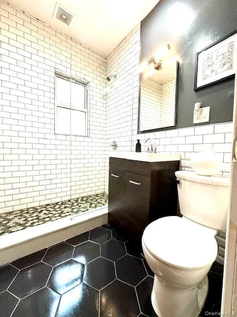 Bathroom featuring tile walls, vanity, dark tile patterned flooring, and a stall shower Bathroom featuring tile walls, vanity, dark tile patterned flooring, and a stall shower