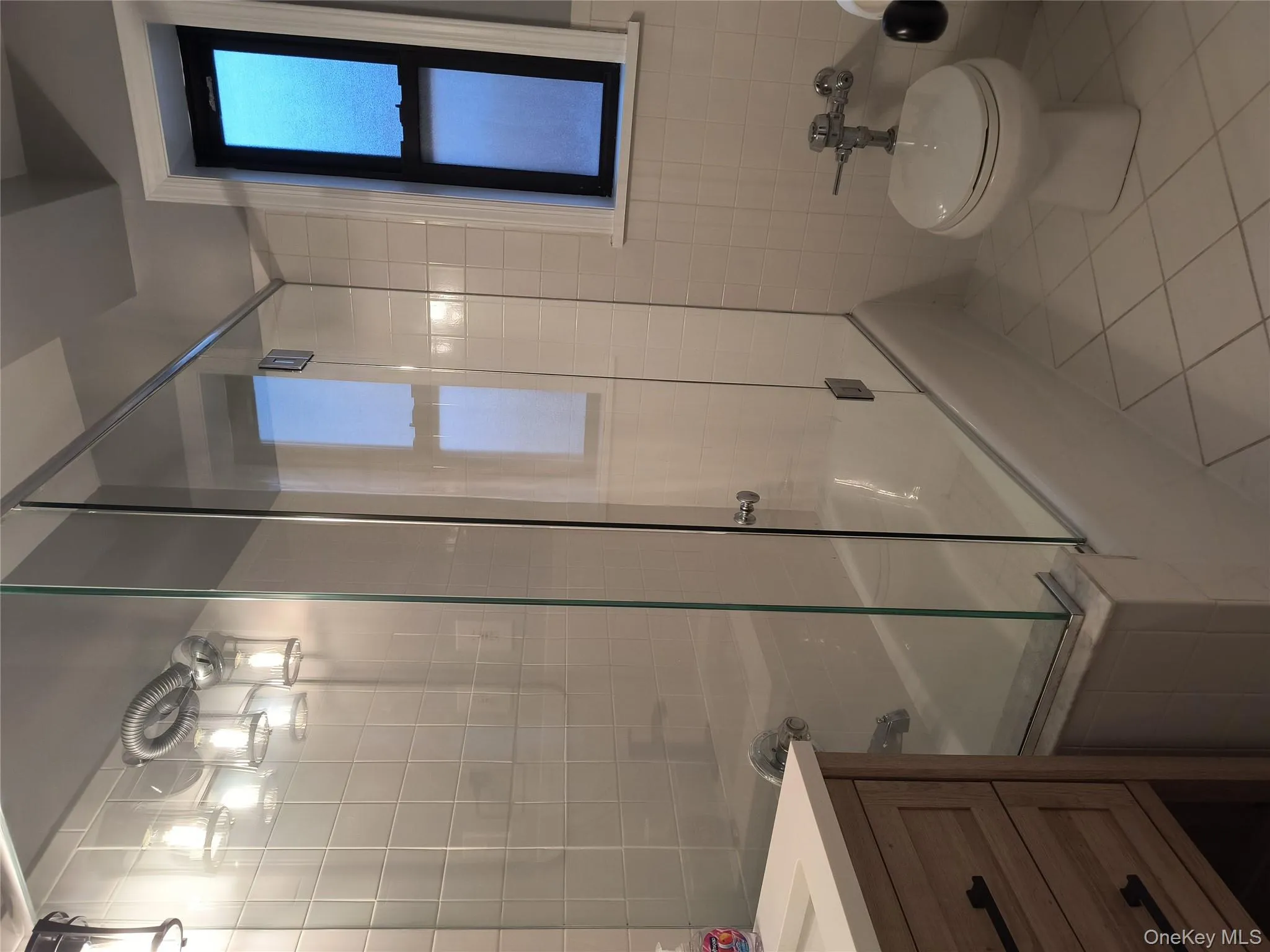 Full bath featuring shower / bath combination with glass door, light tile patterned floors, tile walls, and vanity Full bath featuring shower / bath combination with glass door, light tile patterned floors, tile walls, and vanity