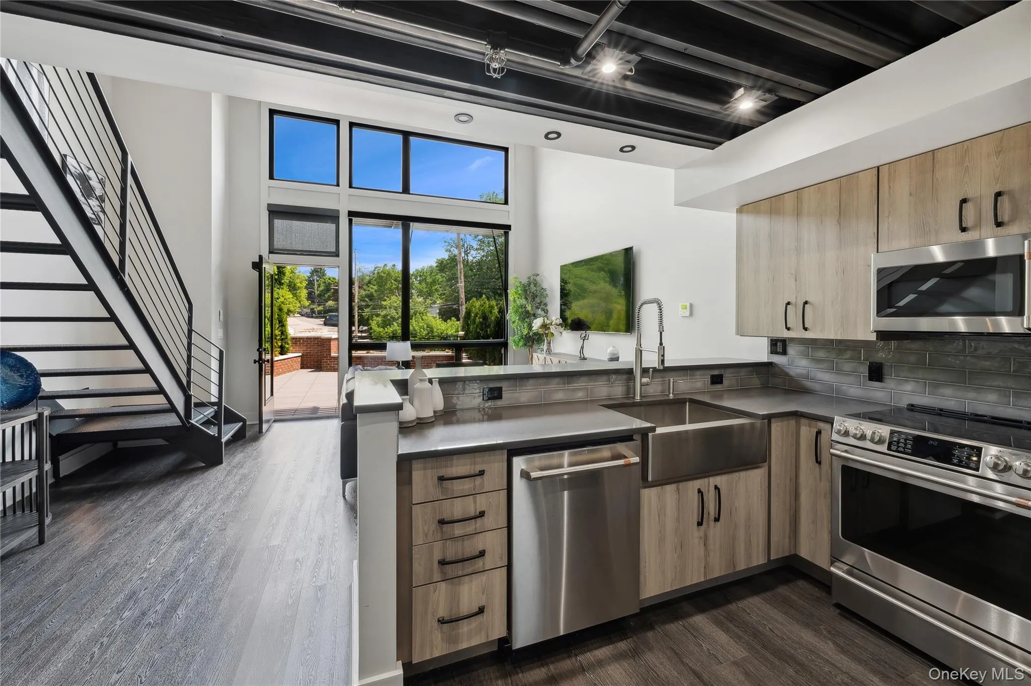 Kitchen with stainless steel appliances, rail lighting, dark countertops, dark wood-style flooring, and a peninsula Kitchen with stainless steel appliances, rail lighting, dark countertops, dark wood-style flooring, and a peninsula