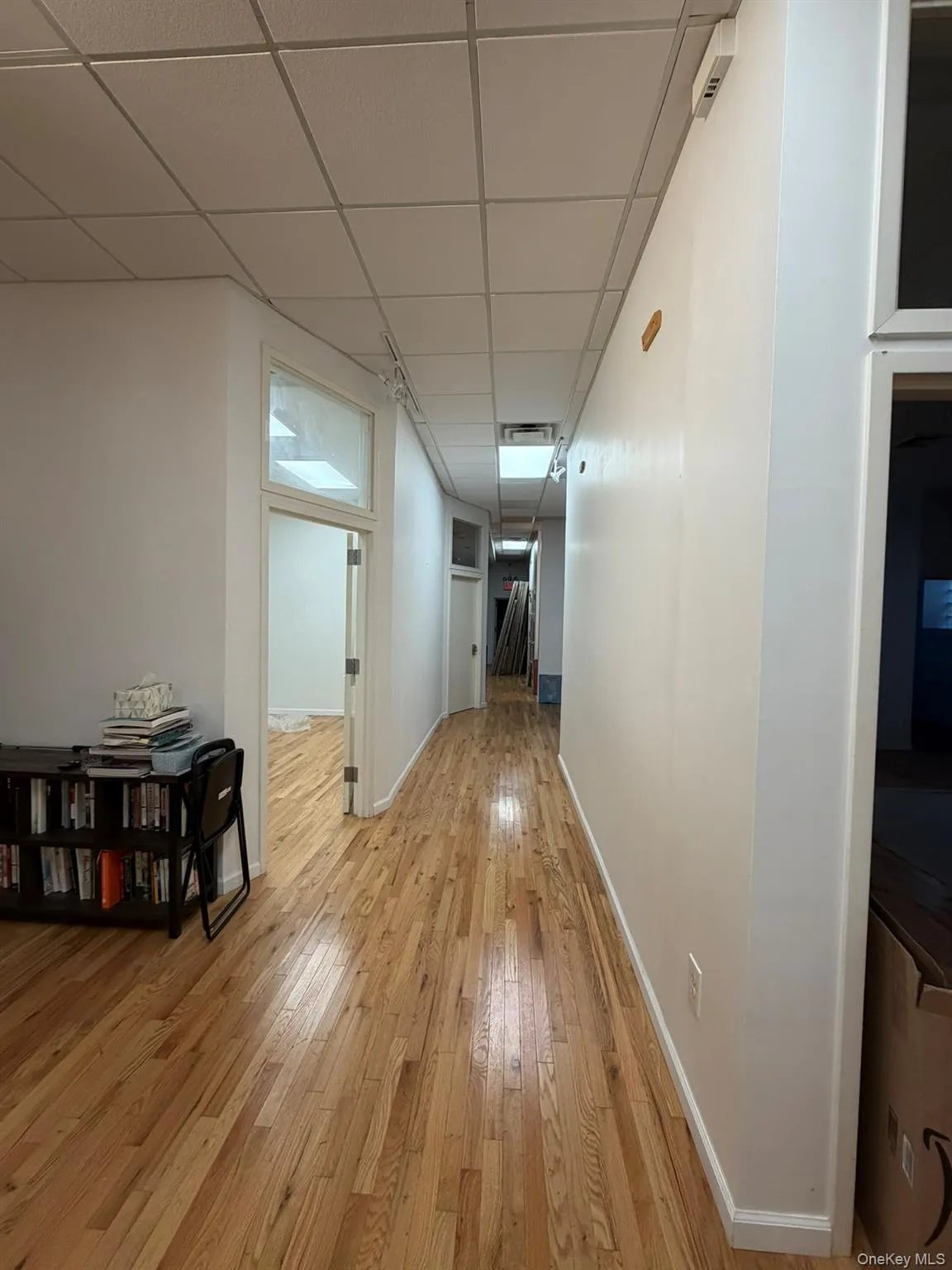 Hallway with light wood-style floors and a paneled ceiling Hallway with light wood-style floors and a paneled ceiling