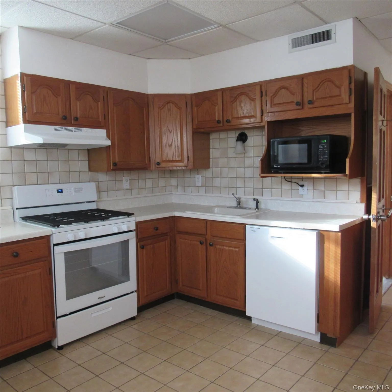 Kitchen with white appliances, brown cabinets, light countertops, under cabinet range hood, and a microwave Kitchen with white appliances, brown cabinets, light countertops, under cabinet range hood, and a microwave