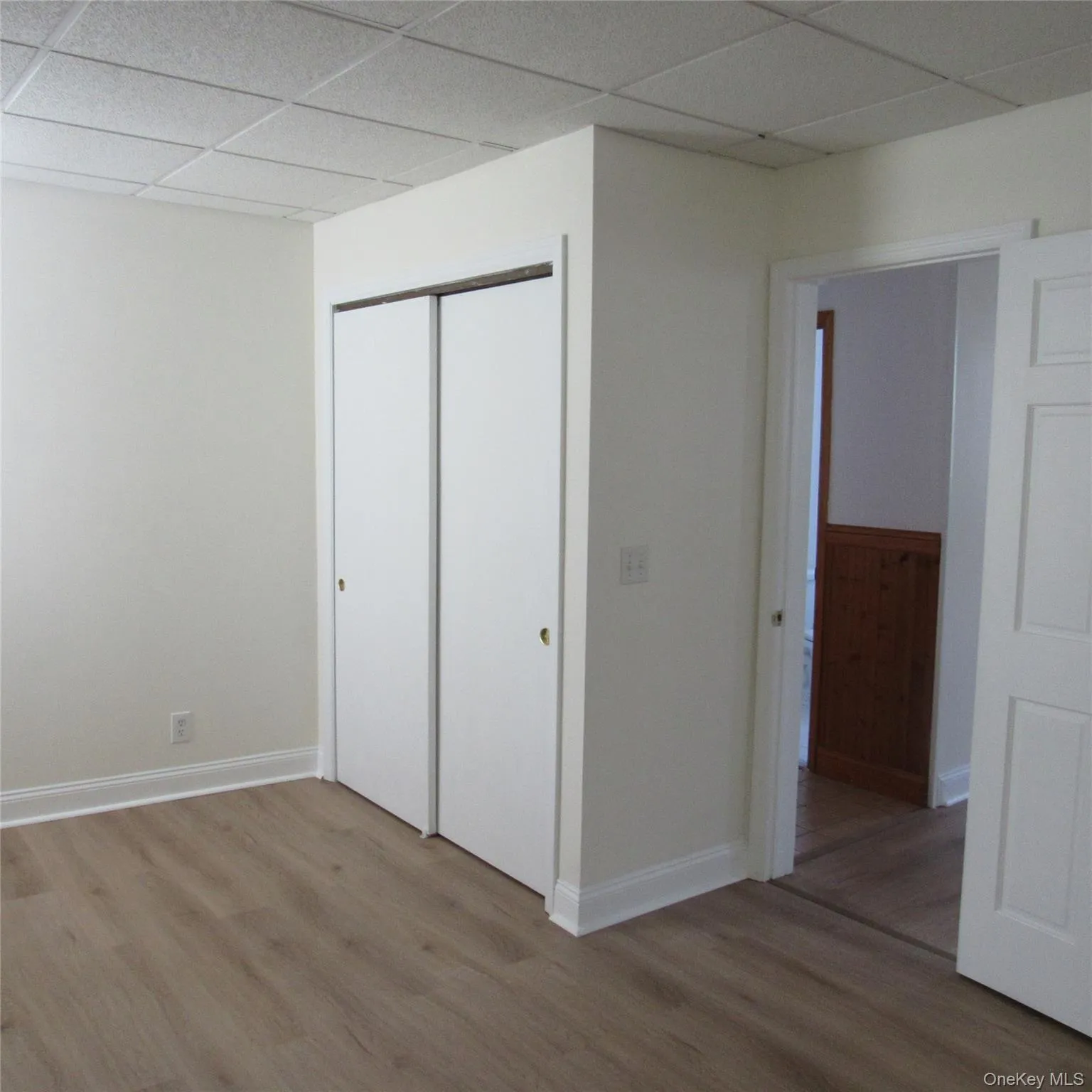 Unfurnished bedroom with a paneled ceiling, light wood-style floors, and a closet Unfurnished bedroom with a paneled ceiling, light wood-style floors, and a closet