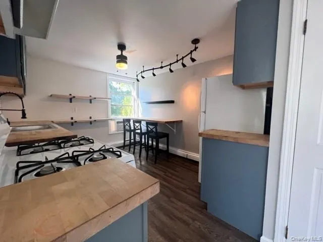 Kitchen featuring white range with gas cooktop, backsplash, butcher block countertops, sink, and dark wood-type flooring with Industrial track lighting. Kitchen featuring white range with gas cooktop, backsplash, butcher block countertops, sink, and dark wood-type flooring with Industrial track lighting.